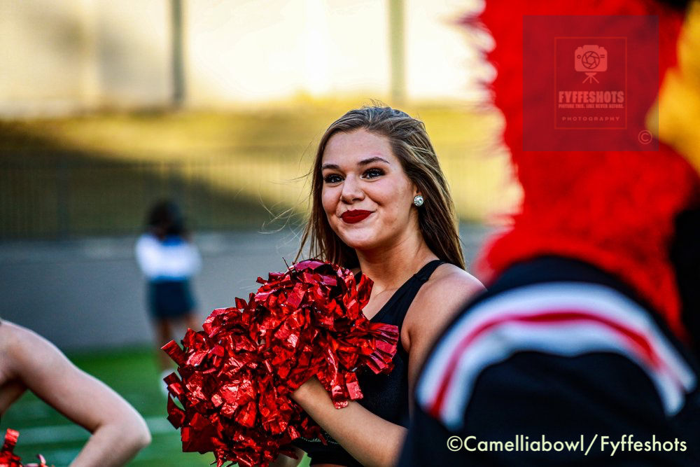 Smiling cheerleader holding red pom-poms during an outdoor performance