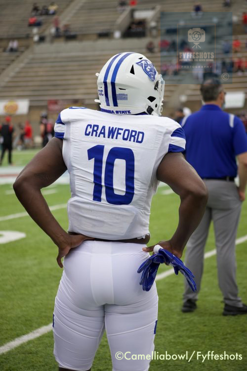 Football player wearing a white and blue uniform with “CRAWFORD” and number 10 on the back, standing on the sideline.
