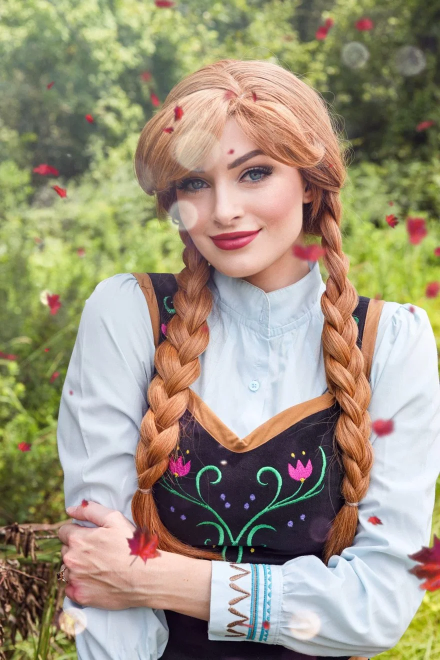 Smiling red-haired woman with braided hair wearing a floral embroidered dirndl in a garden