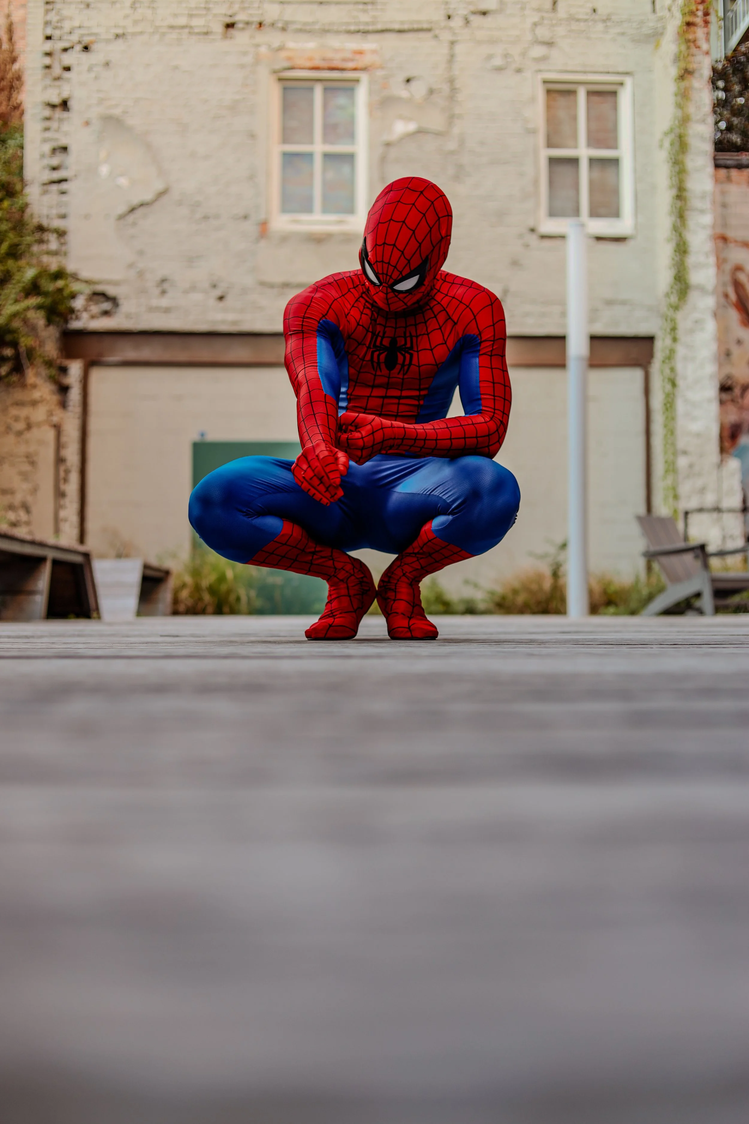 Person in a Spider-Man costume crouching on a wooden platform in front of a weathered building.