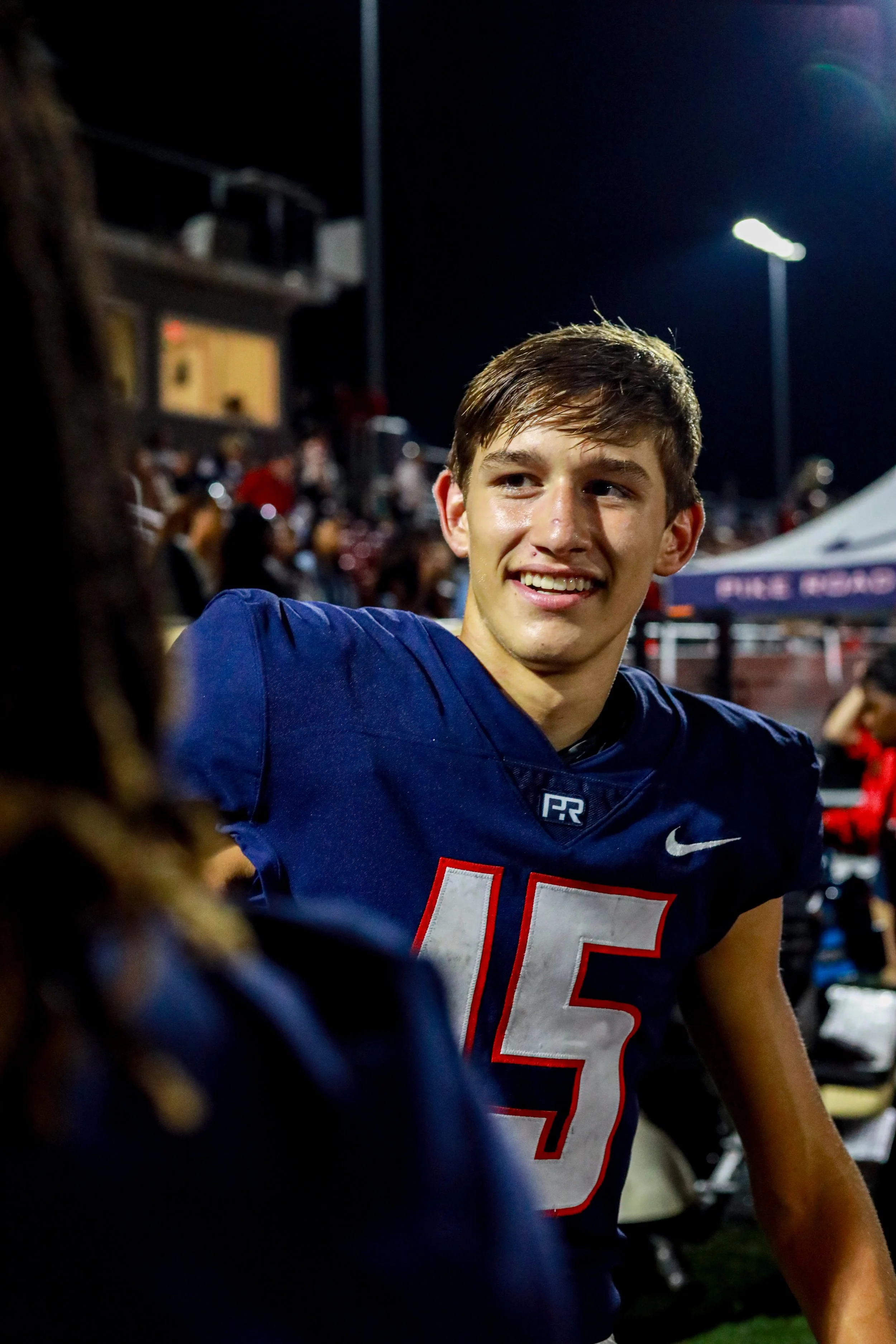 Smiling football player wearing a blue No. 15 jersey in a crowded stadium at night