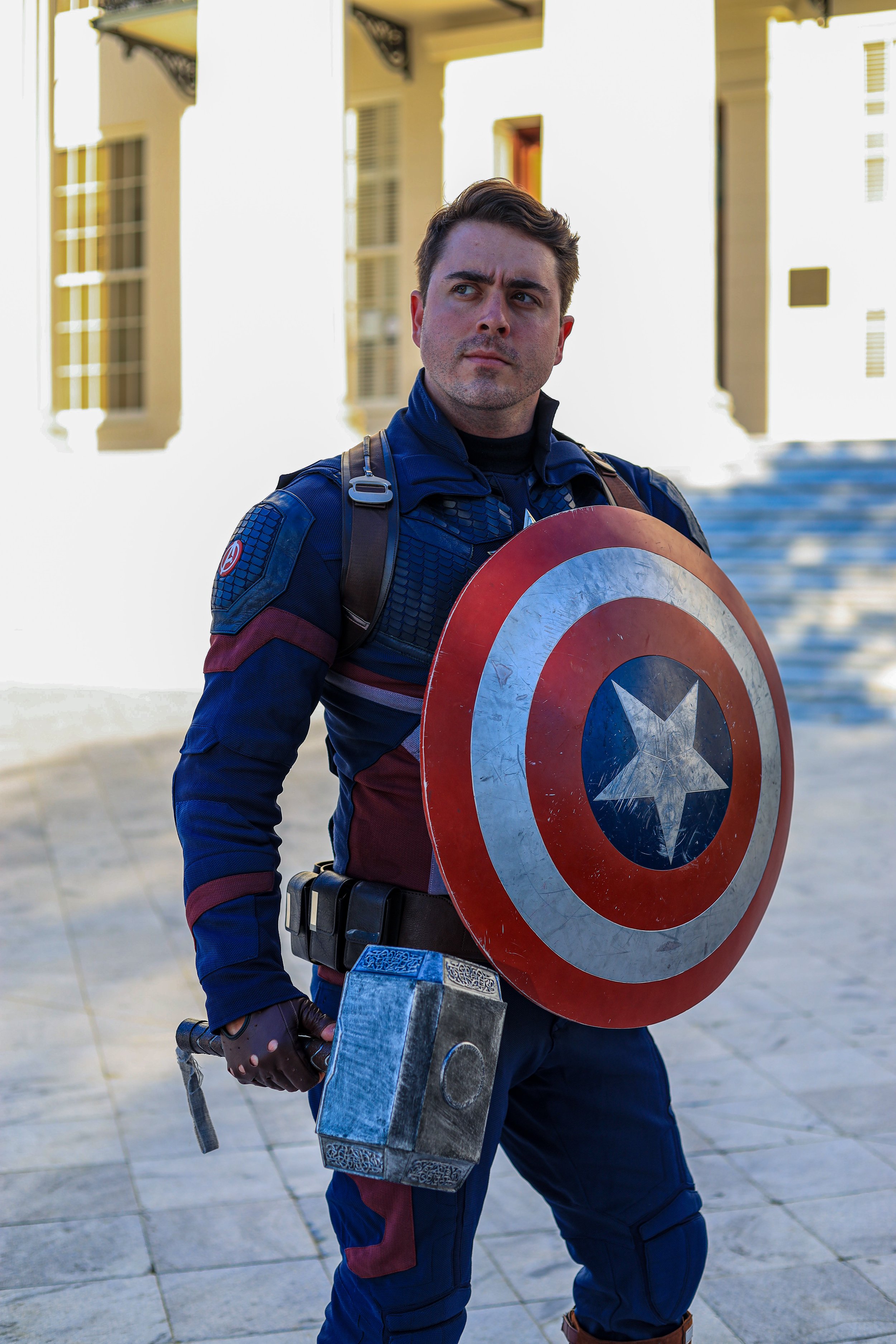 Man dressed as Captain America holding his shield and hammer in a city street