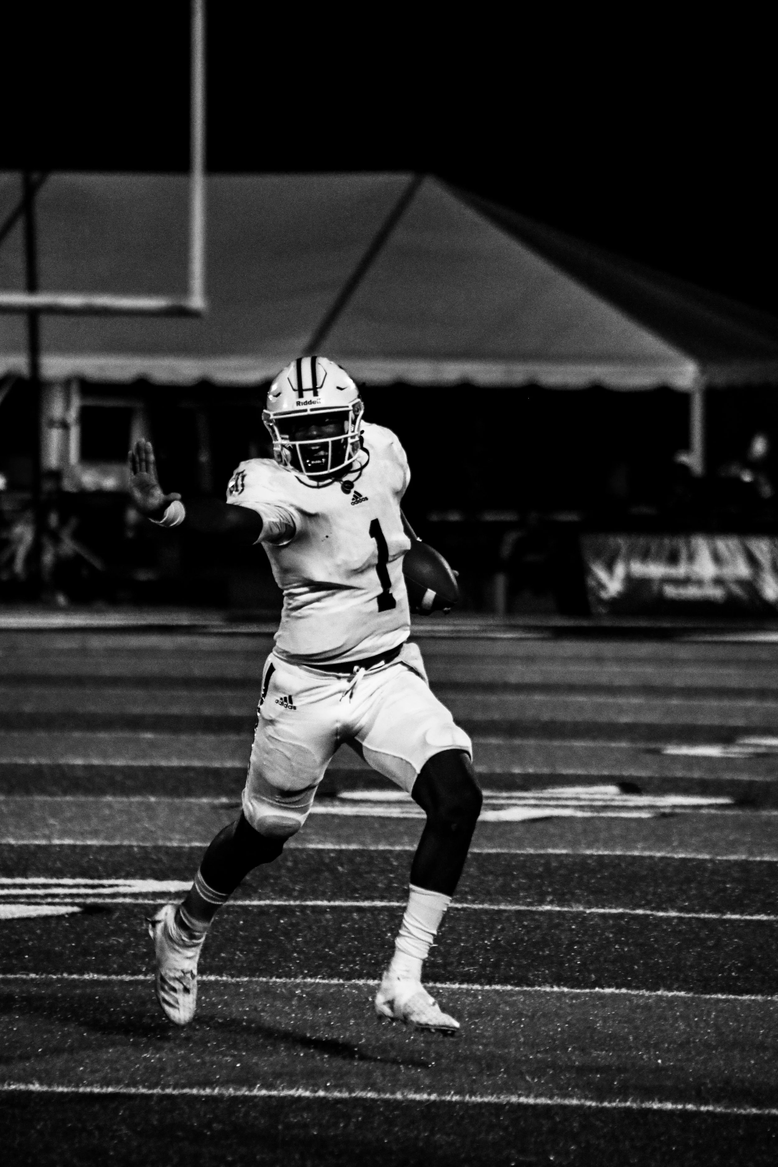Black-and-white photo of a football player in a helmet and uniform running on a field.