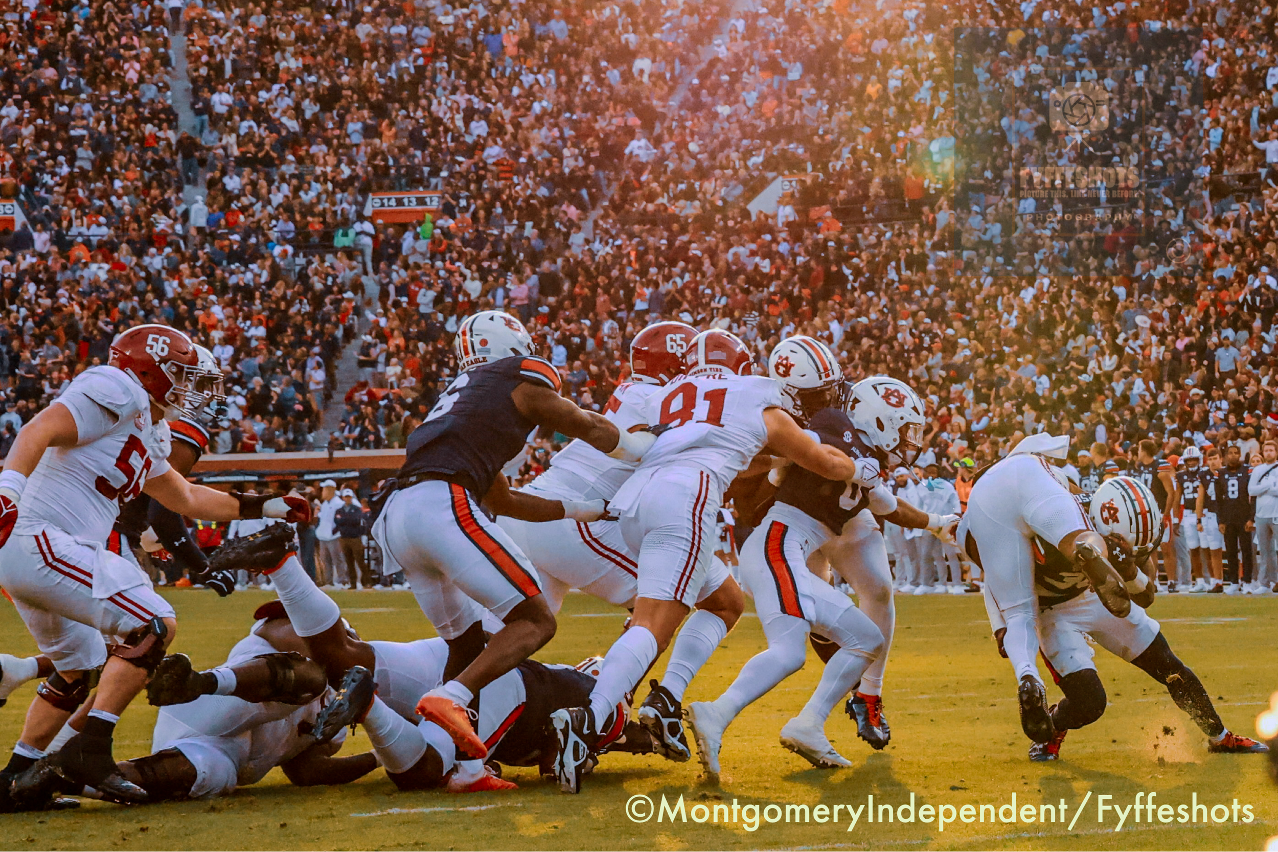 College football game between Auburn Tigers and Alabama Crimson Tide players in action before a packed stadium crowd.
