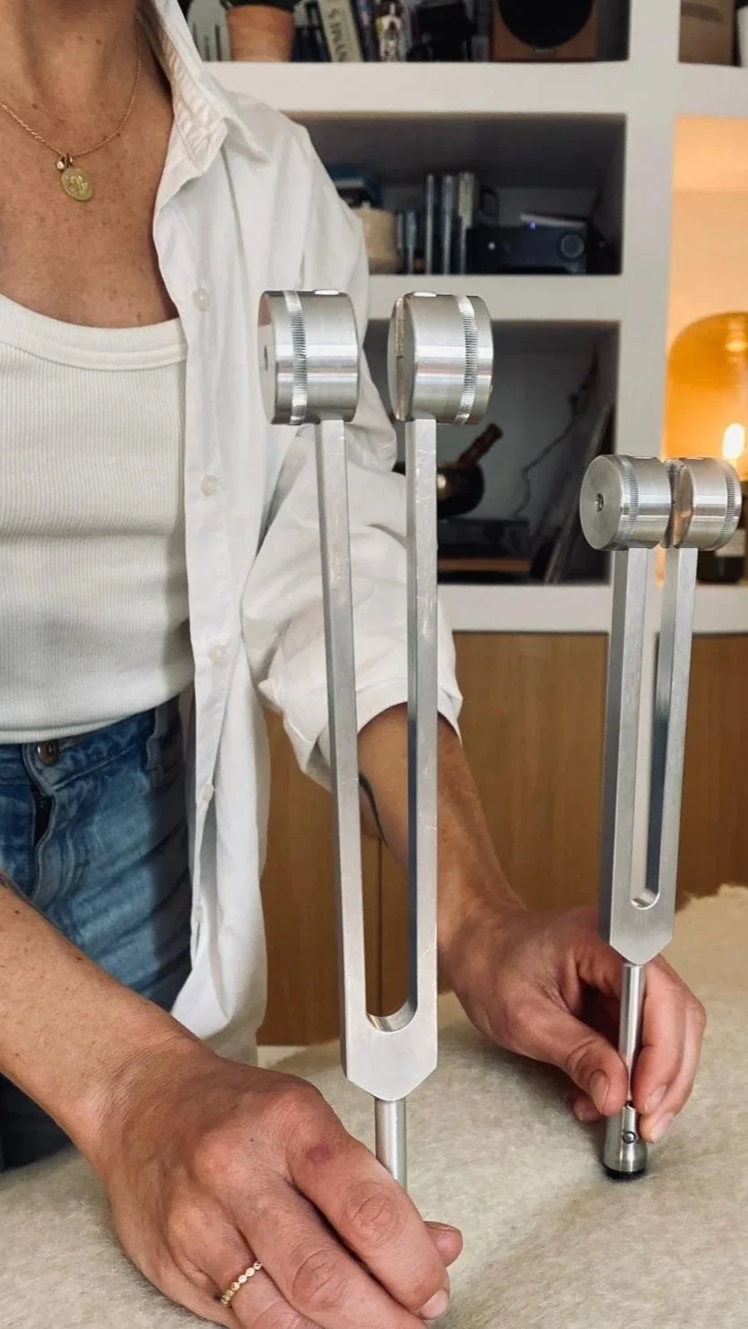 Une femme tient deux instruments de poésie en métal sur une table, avec un livre et des meubles en arrière-plan.
