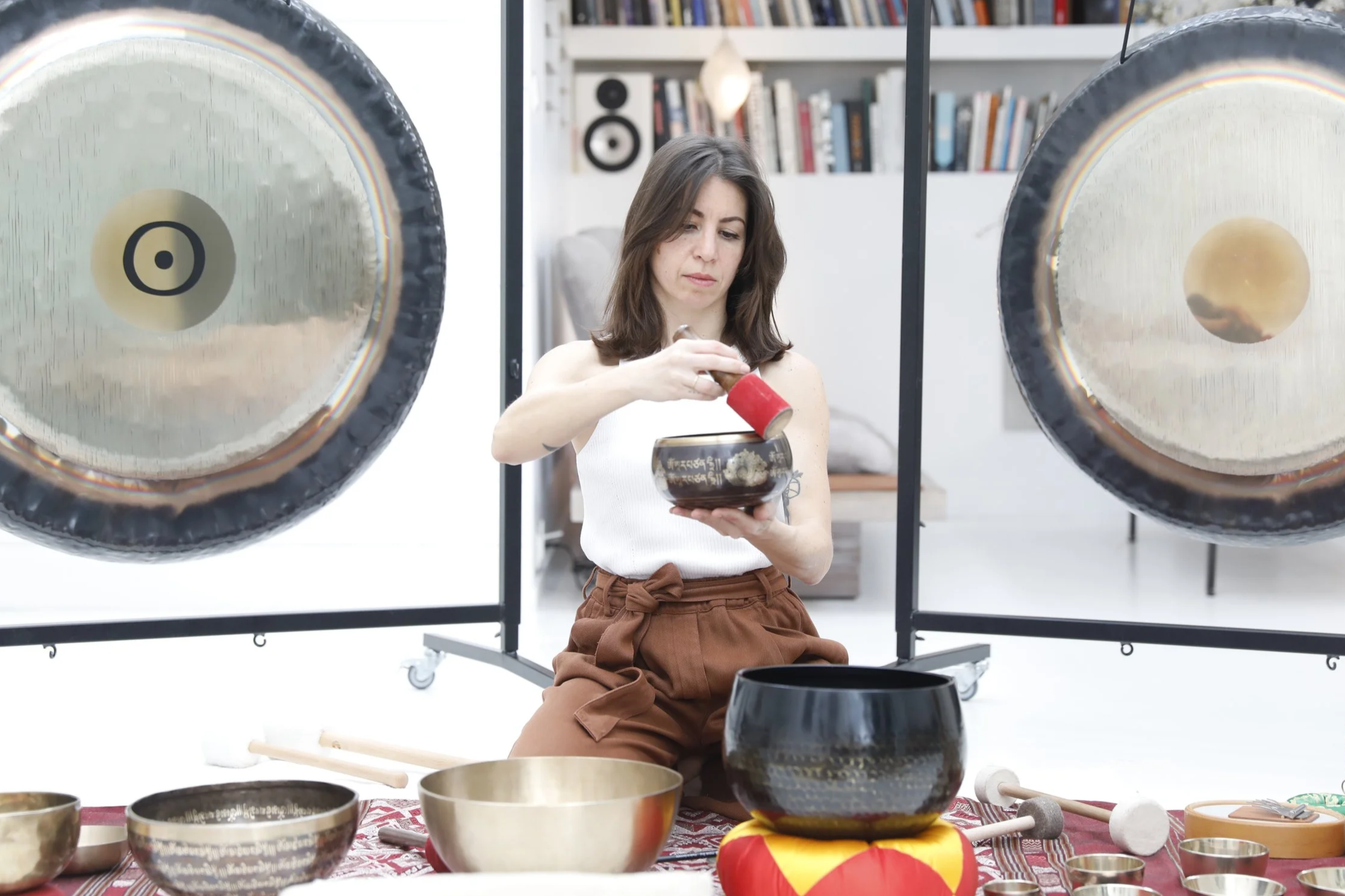 Femme jouant des instruments de percussion dans un studio avec des gongs suspendus et des bols en métal
