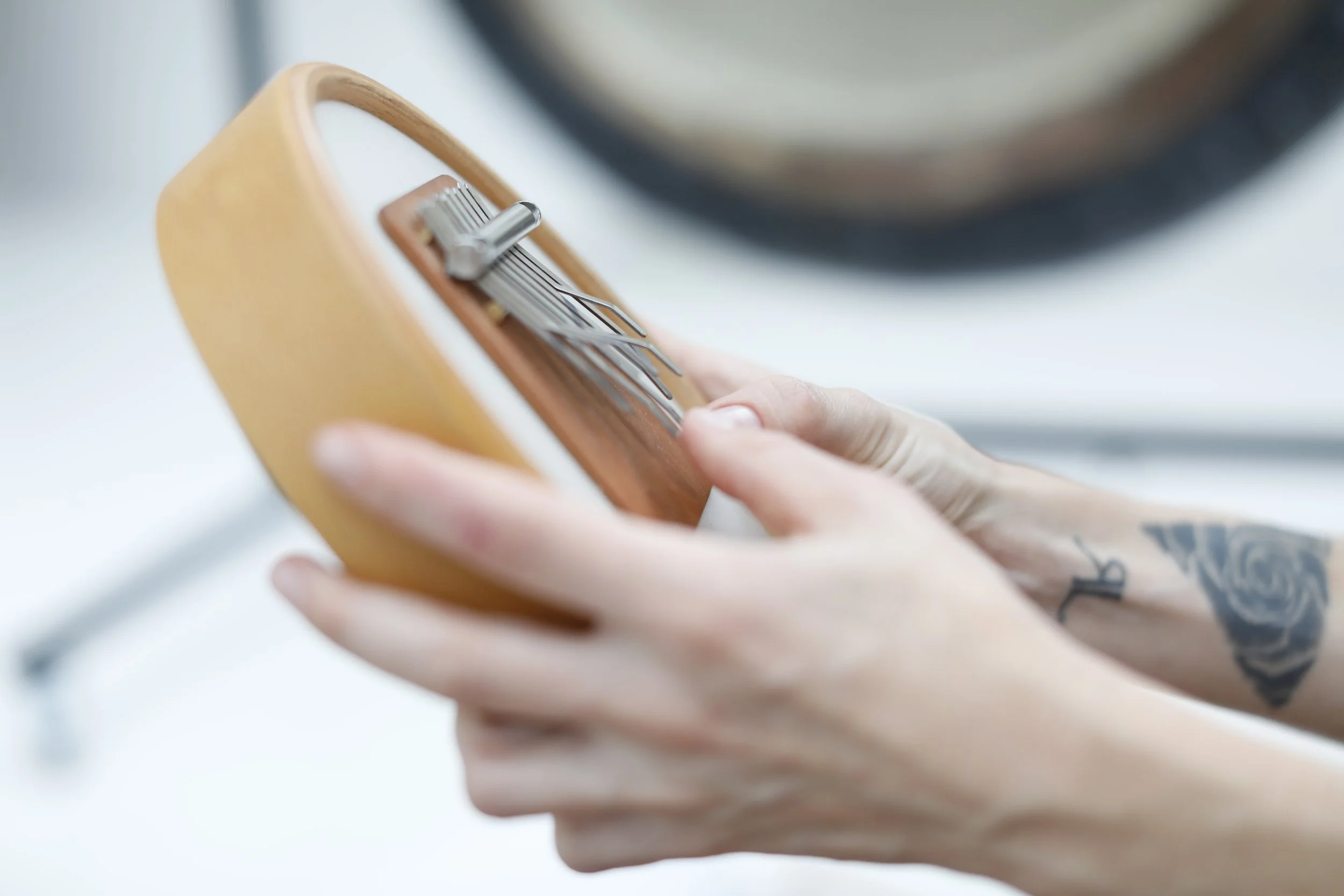 Une main tenant un téléphone avec une coque en bois, zoom sur les doigts et une tattoo, fond flou.