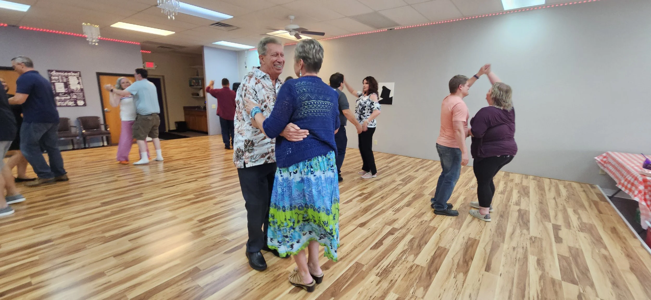 People dancing and socializing in a dance hall with wood flooring and decorated ceiling