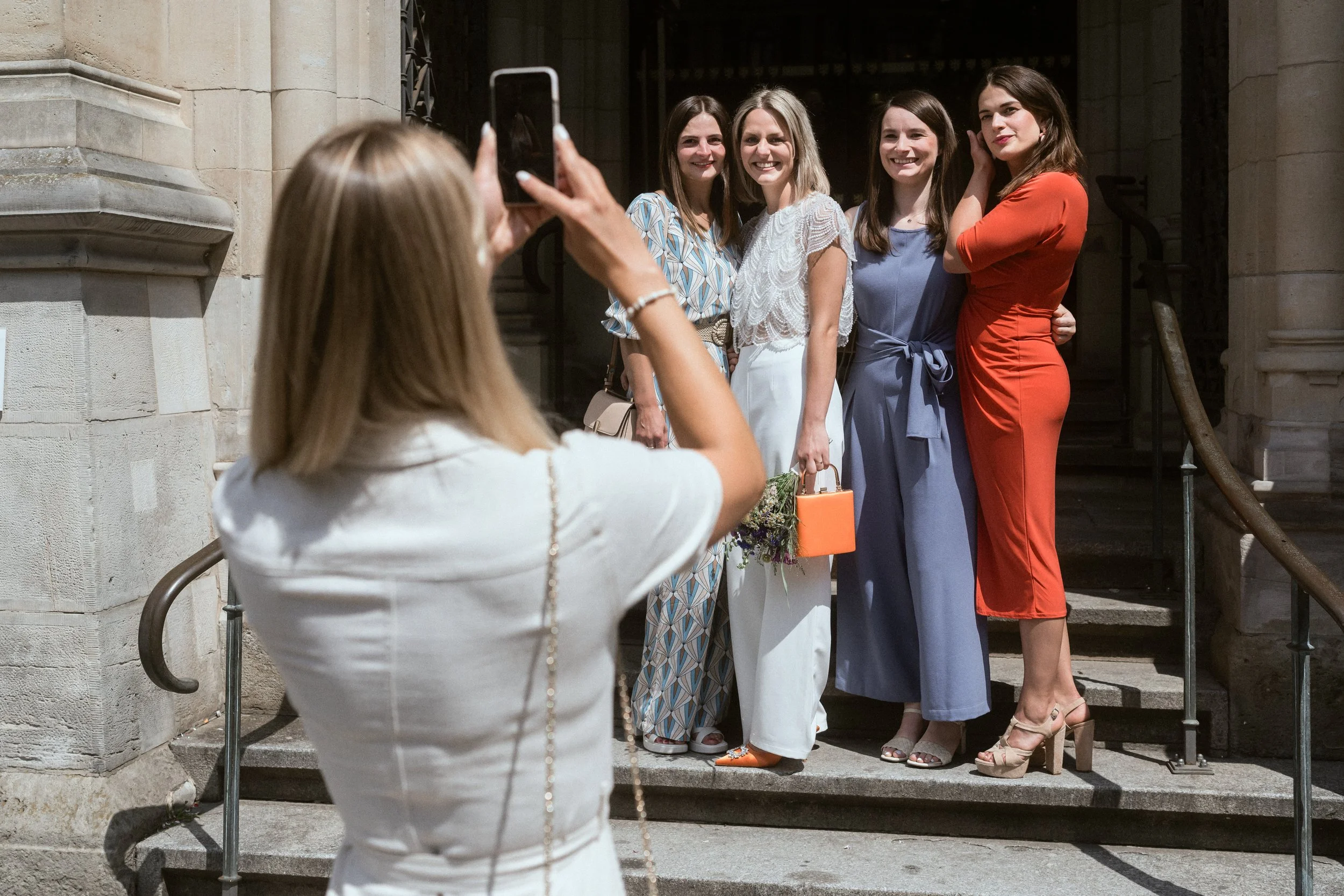 Fünf Frauen posieren auf den Stufen vor einem Gebäude, während eine andere Frau sie fotografiert.