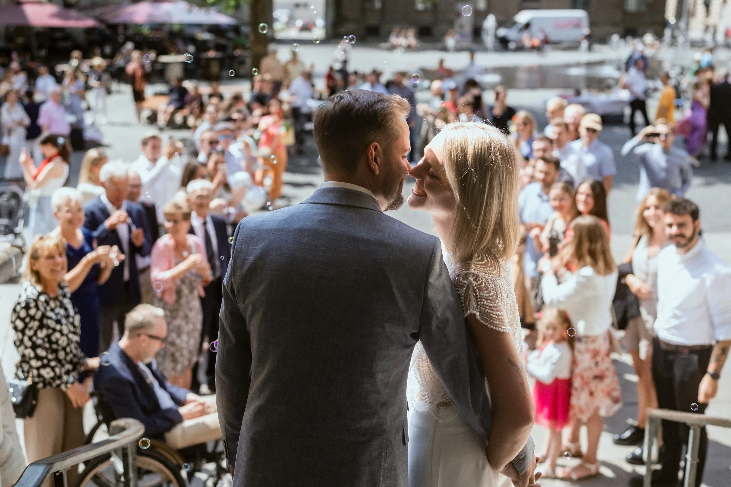 Ein junges Brautpaar bei ihrer Hochzeit tanzt im Freien vor einer großen Menschenmenge, die zuschaut und fotografiert.