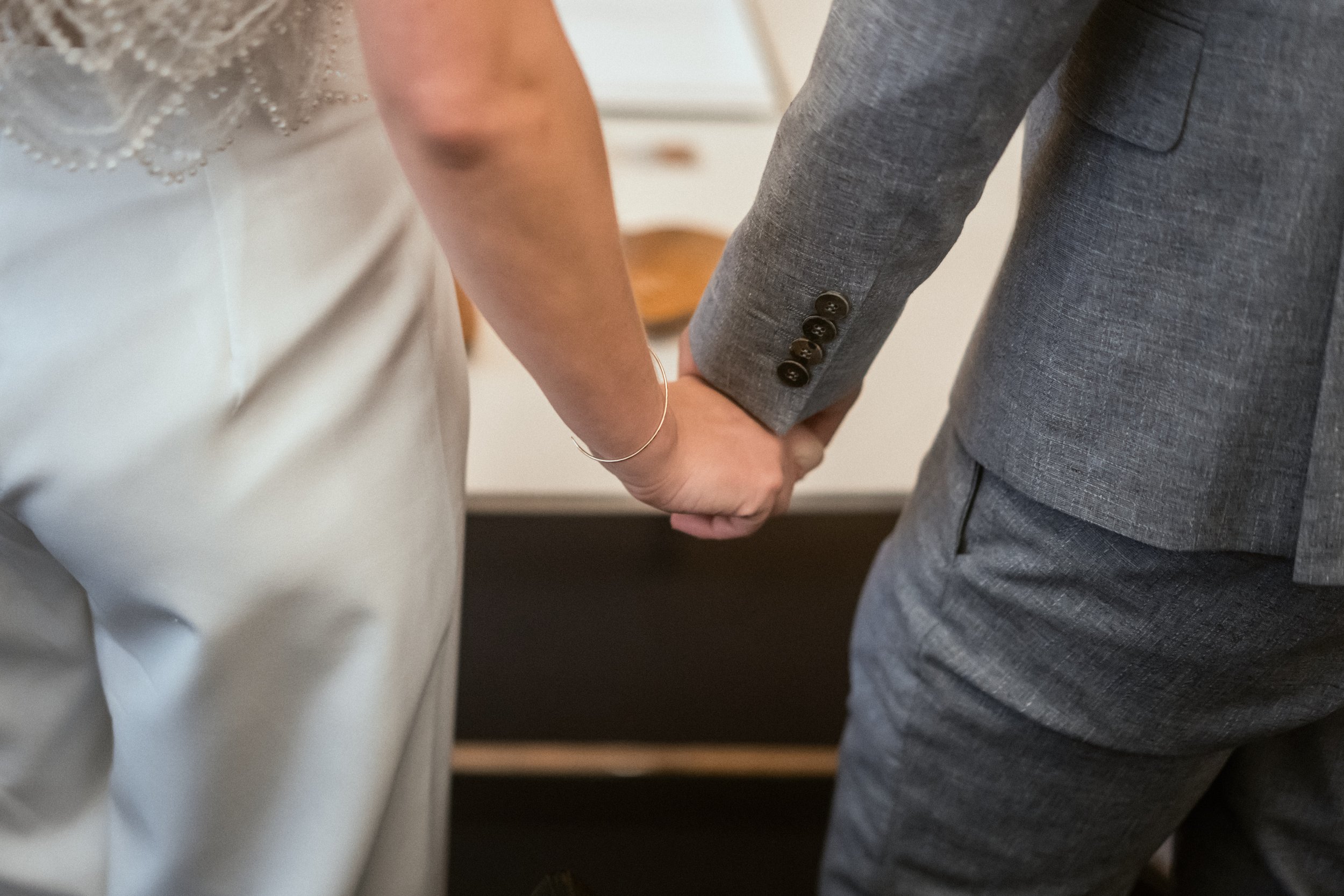 Nahaufnahme von einem Mann in einem grauen Anzug, der eine Frau in einem weißen Kleid berührt, während sie Hand in Hand stehen.