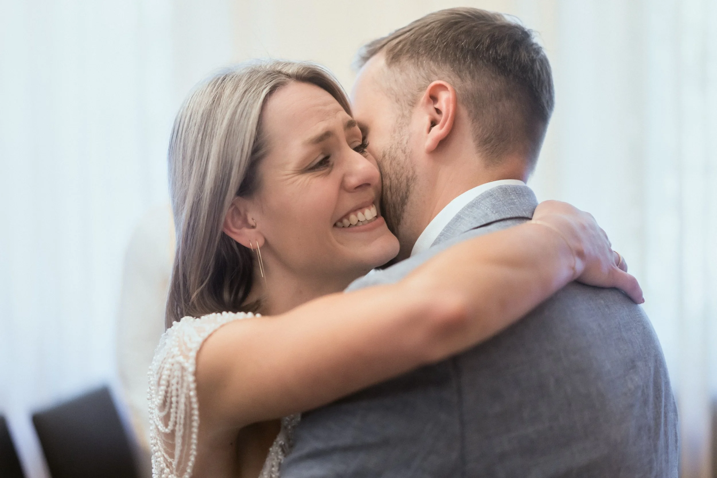 Ein Mann und eine Frau umarmen sich beim Tanzen bei einer Hochzeit. Die Frau lächelt glücklich, während sie den Mann umarmt.