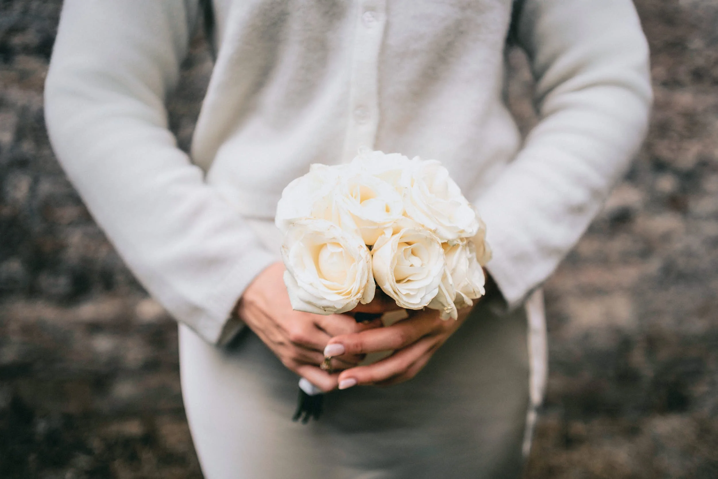 Eine Person in einem hellen Hemd hält einen großen Blumenstrauß aus weißen Rosen.