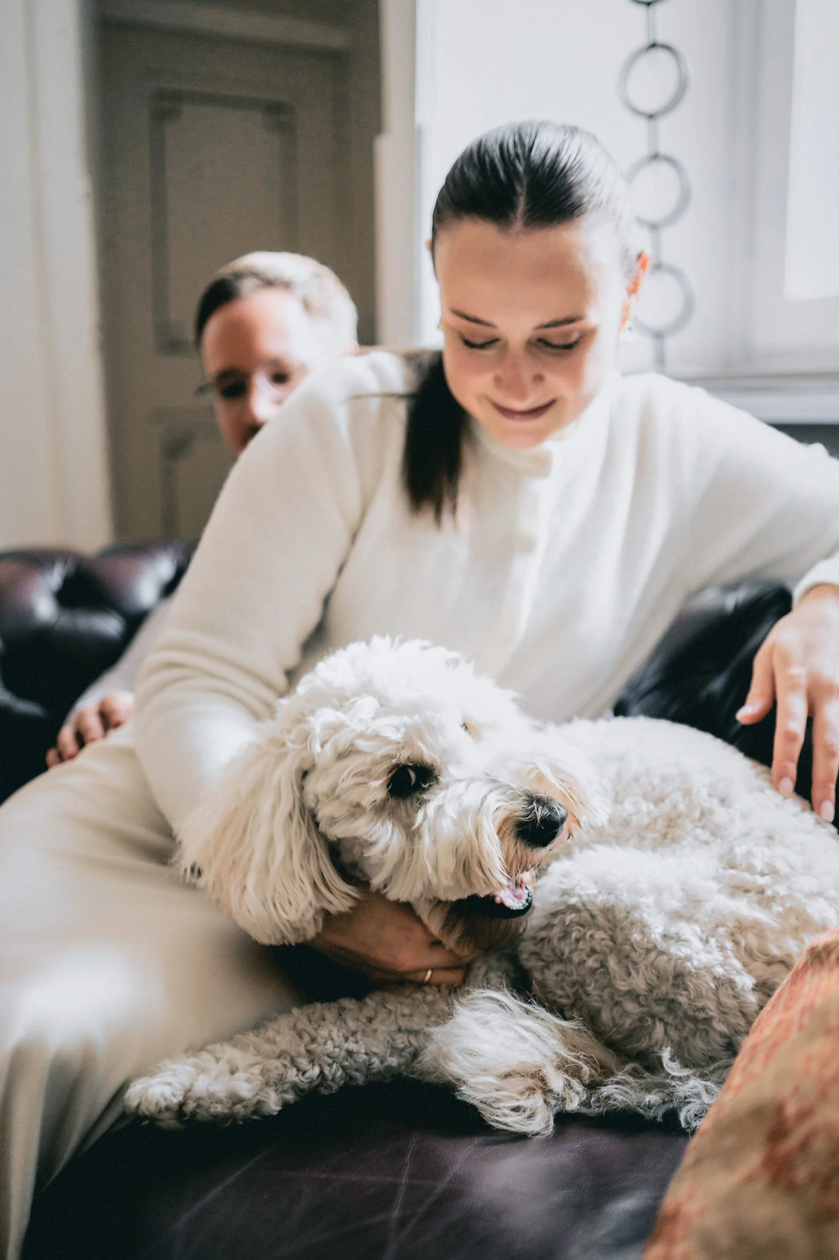 Zwei Menschen, eine Frau und ein Kind, spielen mit einem großen weißen Hund auf einem Sofa im Wohnzimmer.