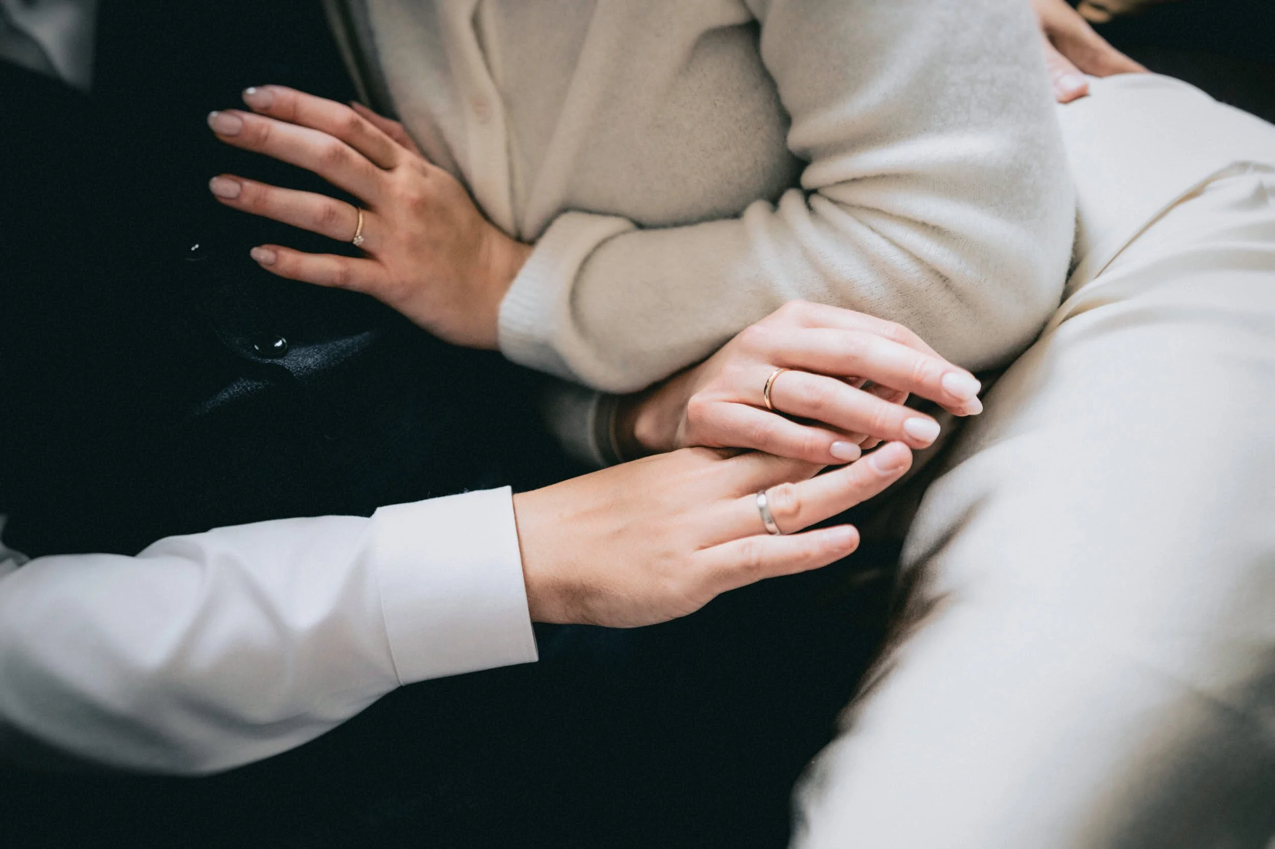 Mehrere Hände berühren einen Arm, die Person trägt eine beige Strickjacke und mehrere Ringe.
