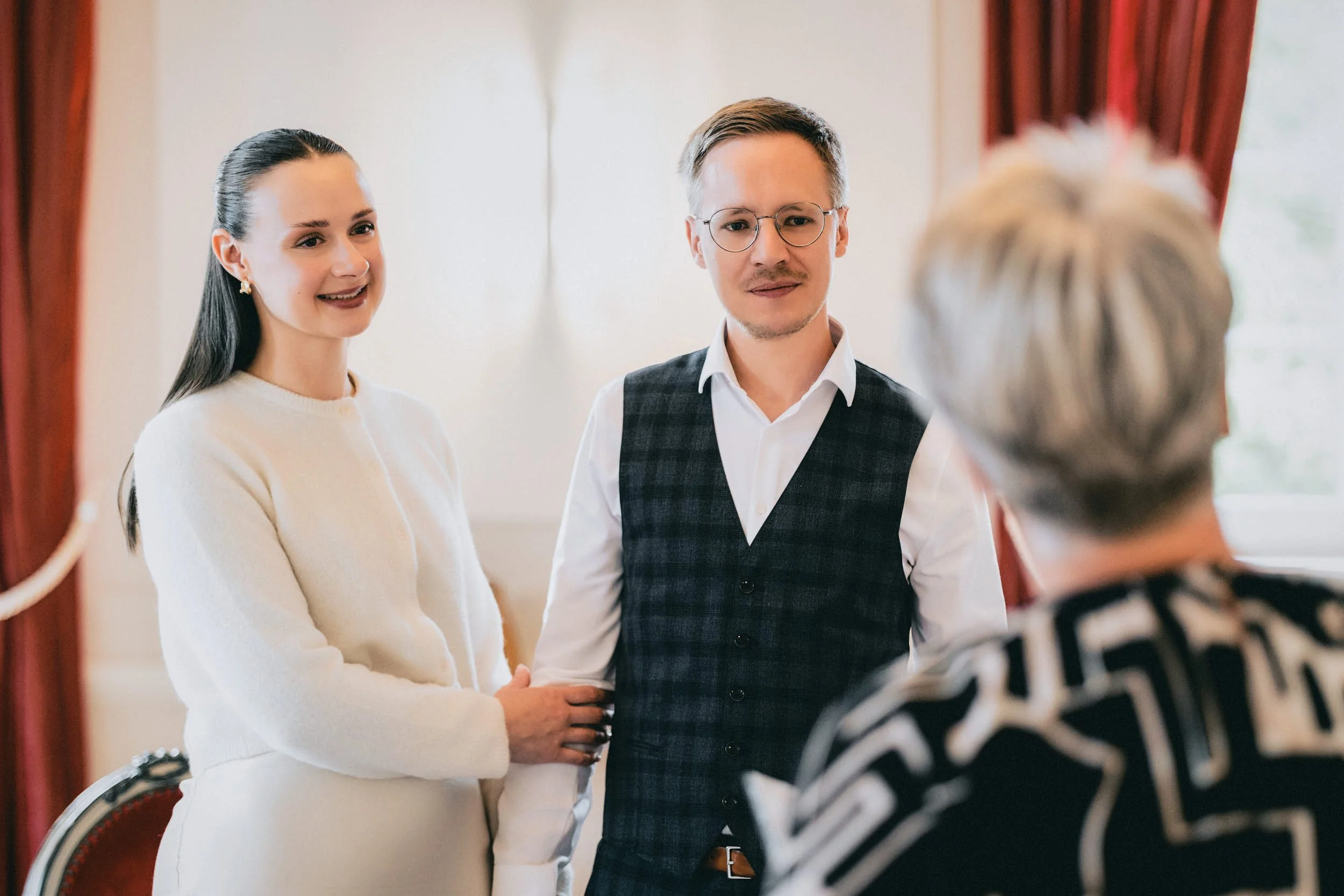 Drei Menschen im Gespräch, eine Frau links, ein Mann Mitte mit Brille und eine ältere Frau rechts. Es scheint ein formelles Treffen zu sein.