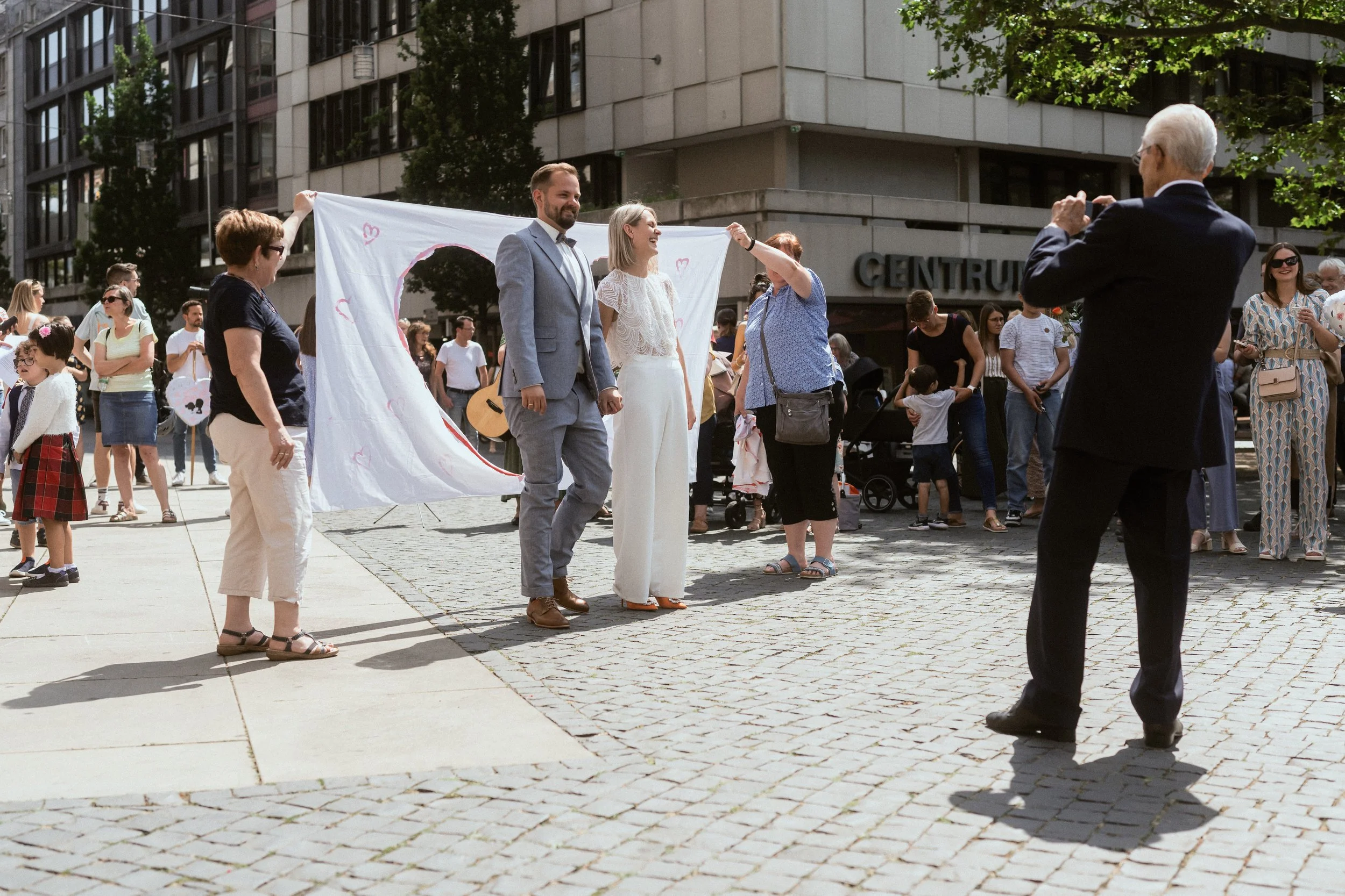 Menschen bei einer Demonstration oder Feier im Stadtzentrum, einige halten Schilder hoch, andere fotografieren die Szene.