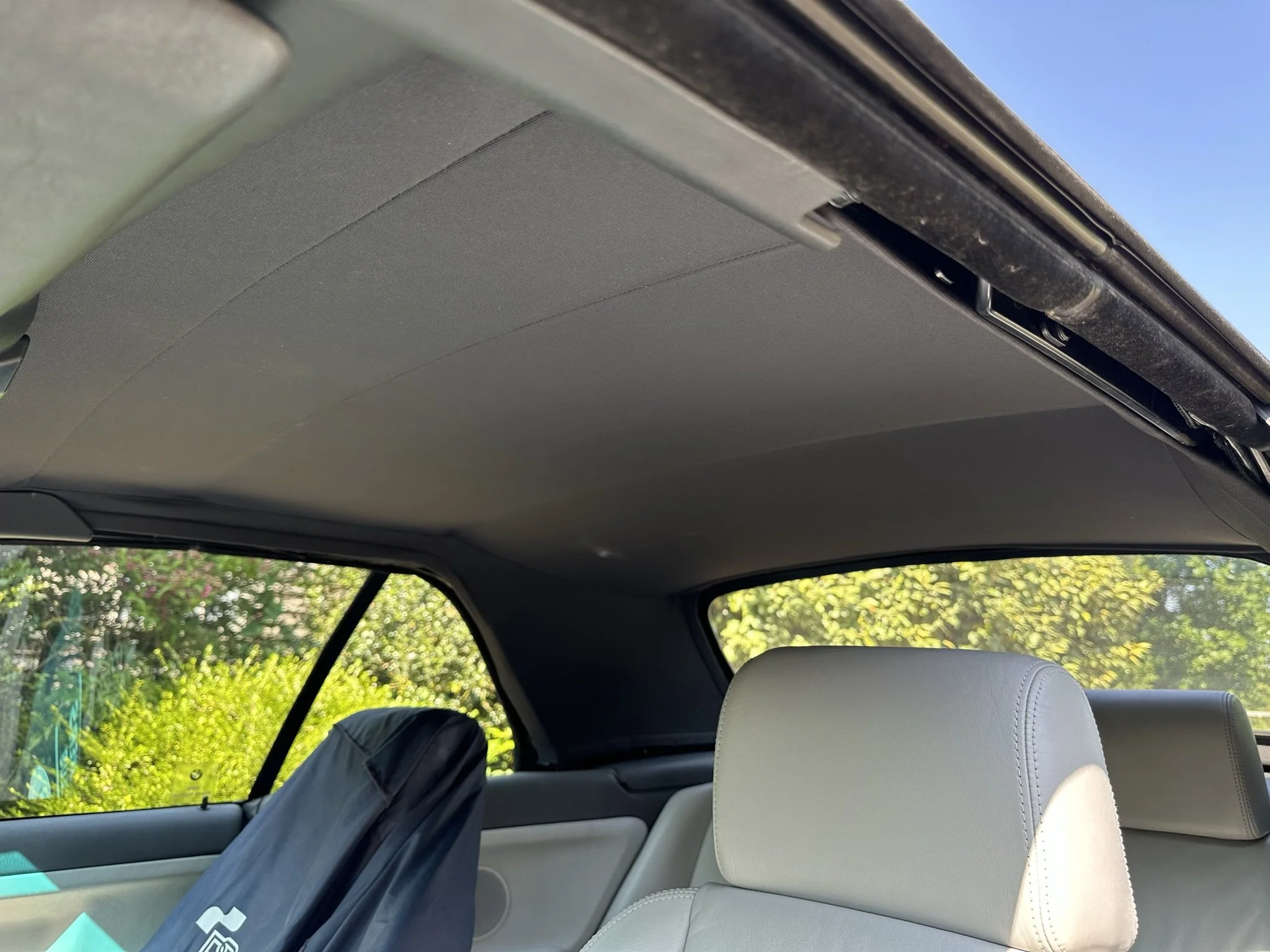 View of the interior of a car, showing the grey headliner, the back of grey seats, a window with a view of greenery outside, Bmw E36 M3 Convertible Headlining