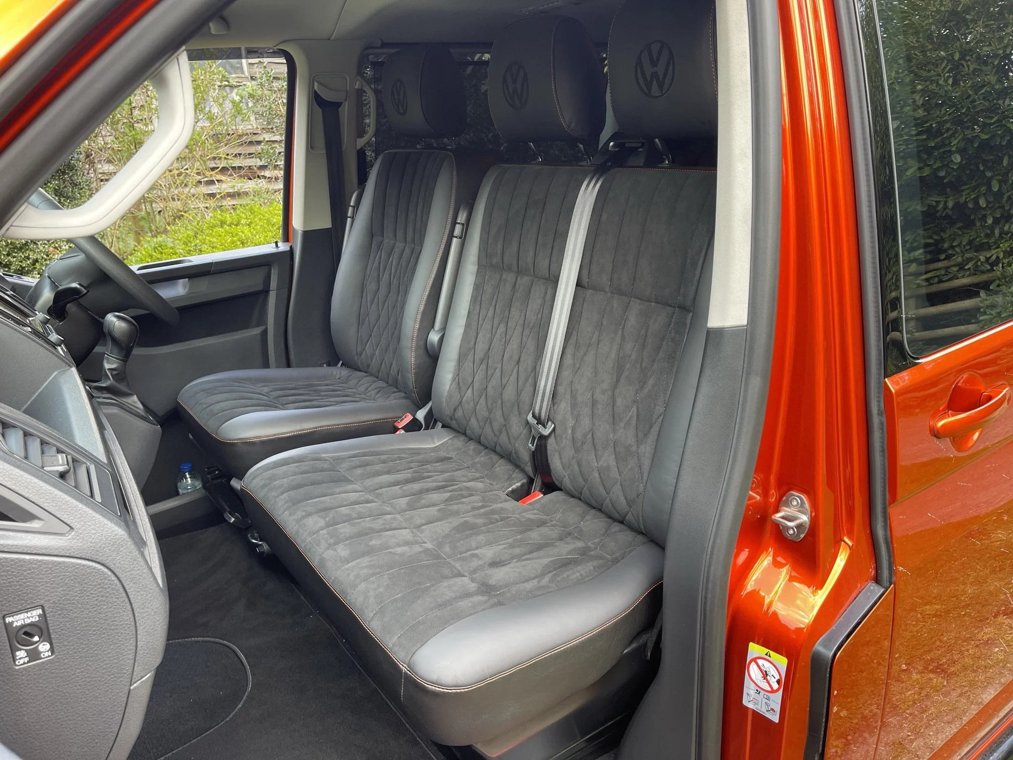 Interior of a red Volkswagen van, showing the front passenger and rear seats with black upholstery, headrests, and seat belts.