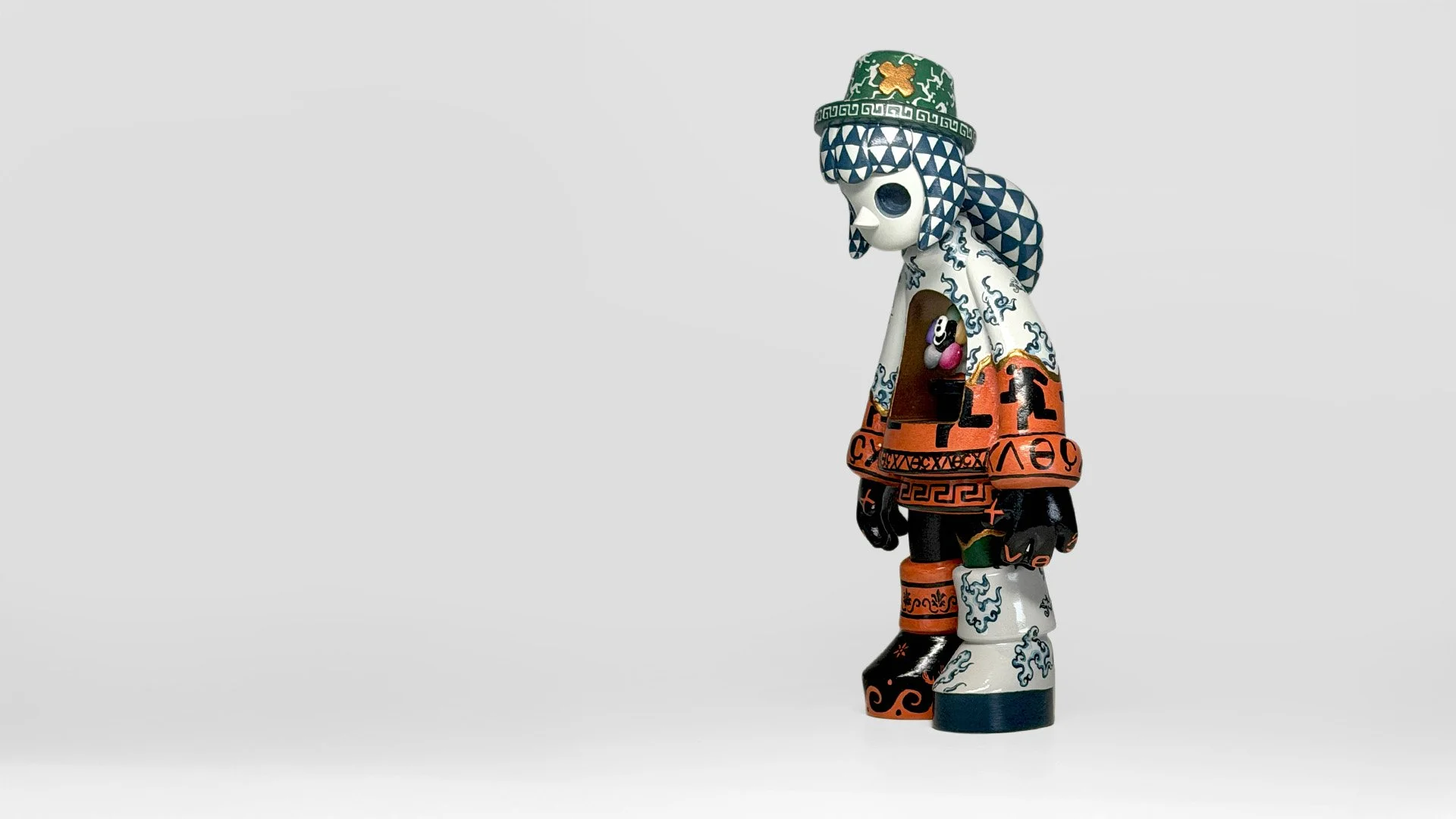 Miss Bliss art toy by Yoshihito, featuring a bowed figure with intricate blue, orange, green and gold patterns and a miniature character inside its chest.