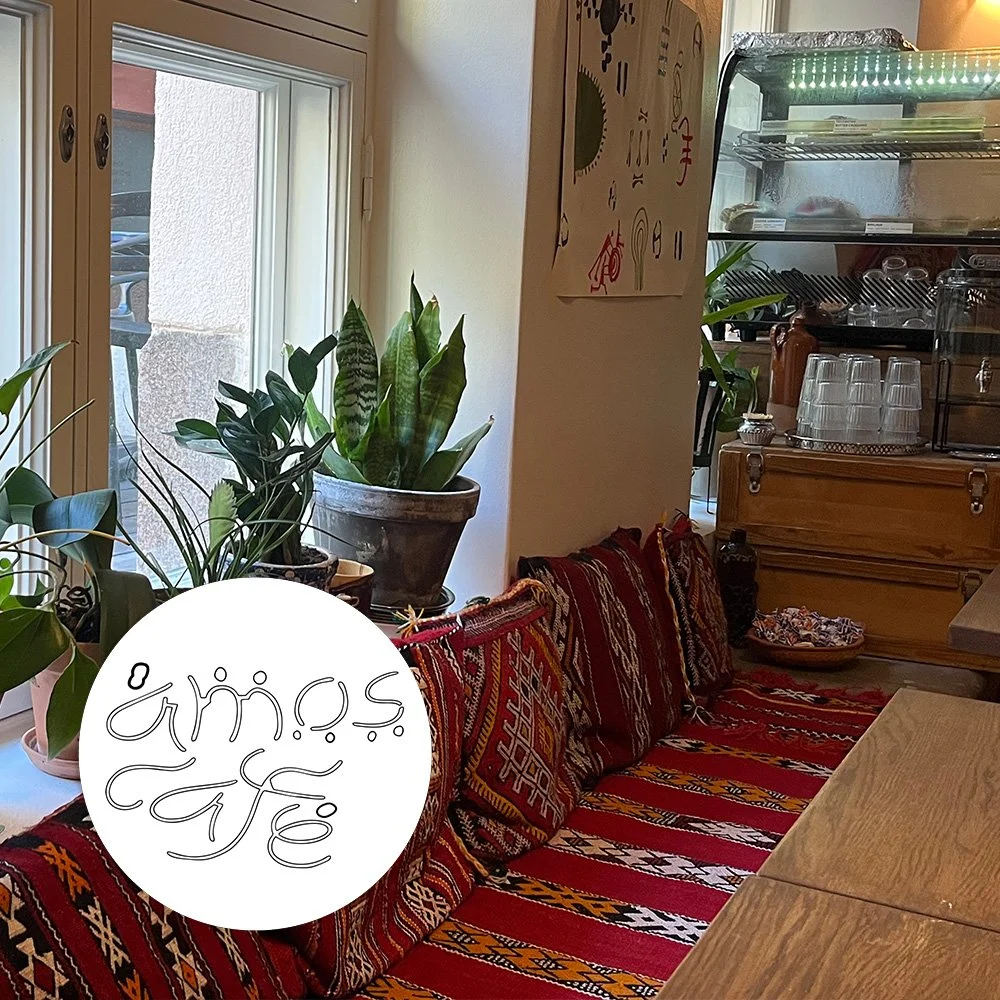 Interior of Amos Café in Helsinki with patterned seating, houseplants and a round café sign.