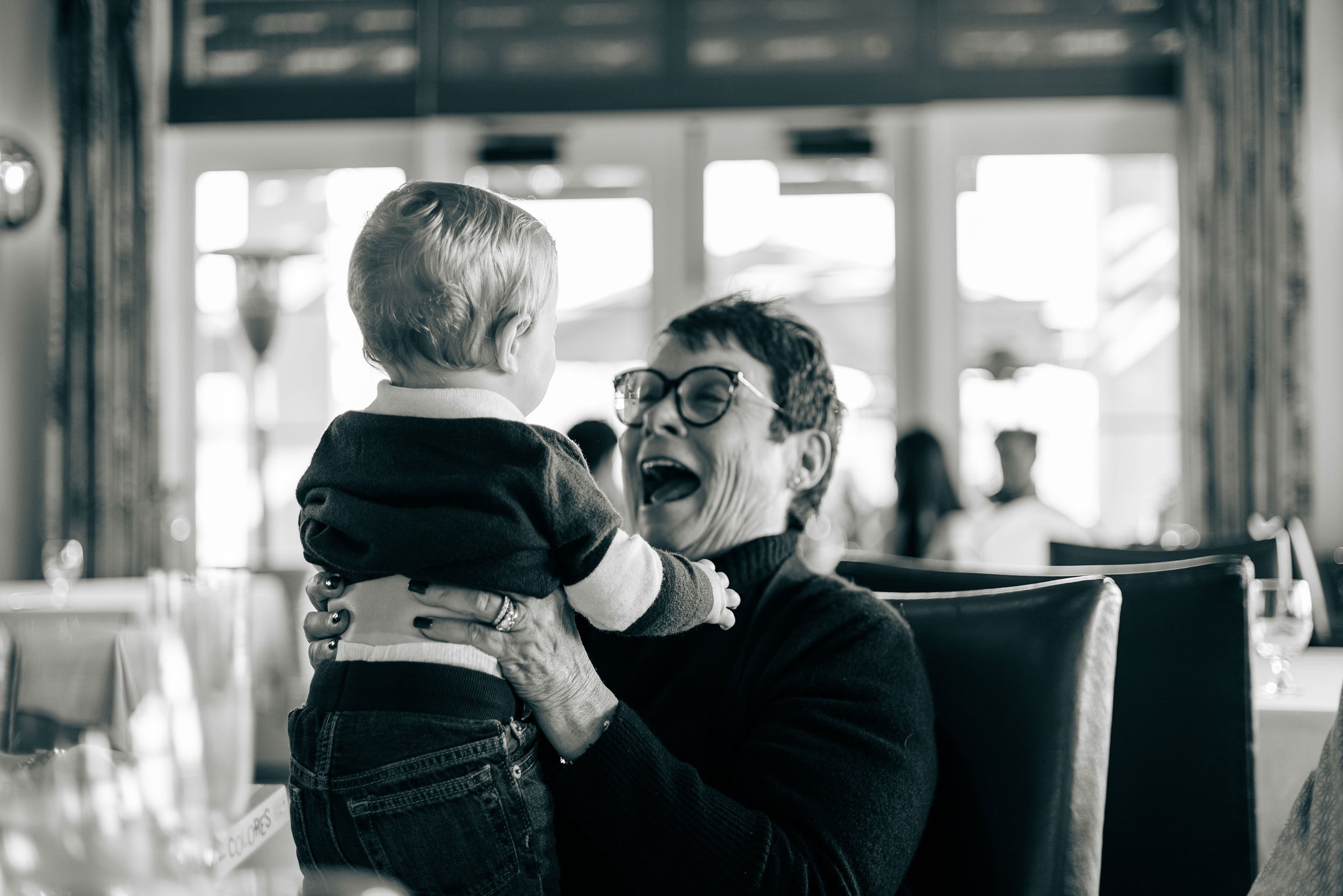 A joyful older woman holding a small child in a restaurant setting.