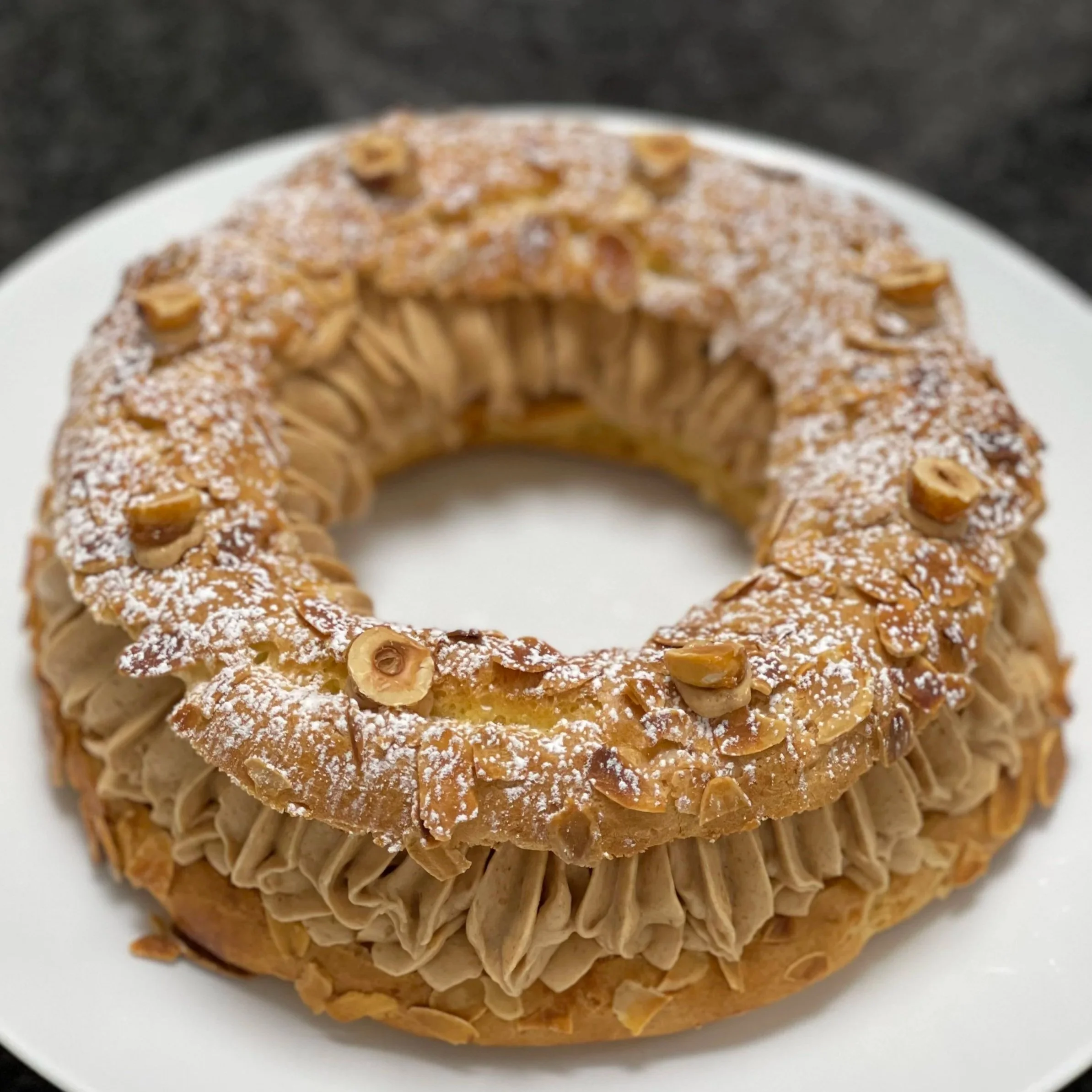 A homemade Paris-Brest on a plate, filled with praline buttercream and a pure praline core, dusted with powdered sugar