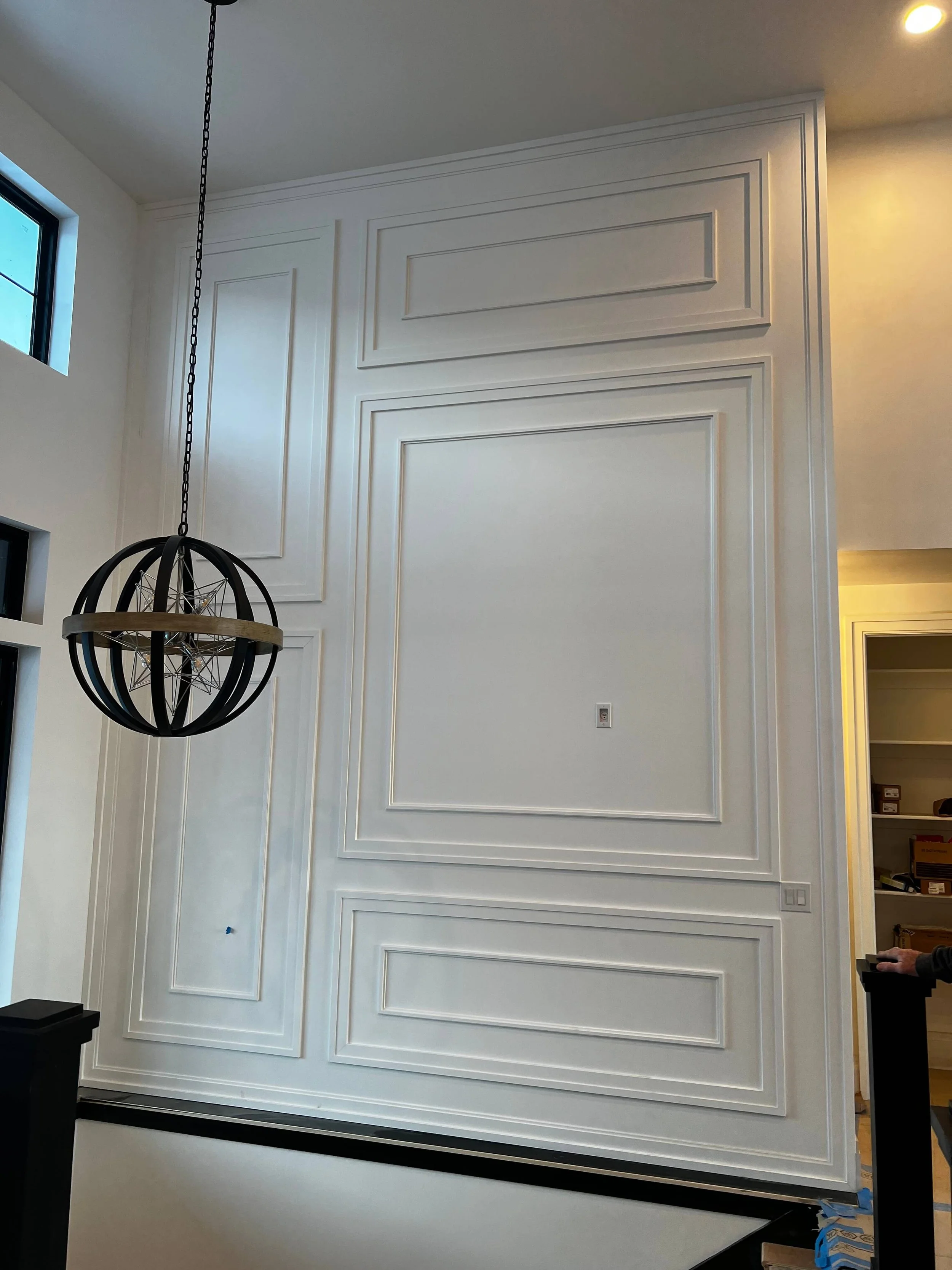 Custom white wall with decorative molding and a hanging black spherical chandelier in a modern interior space.