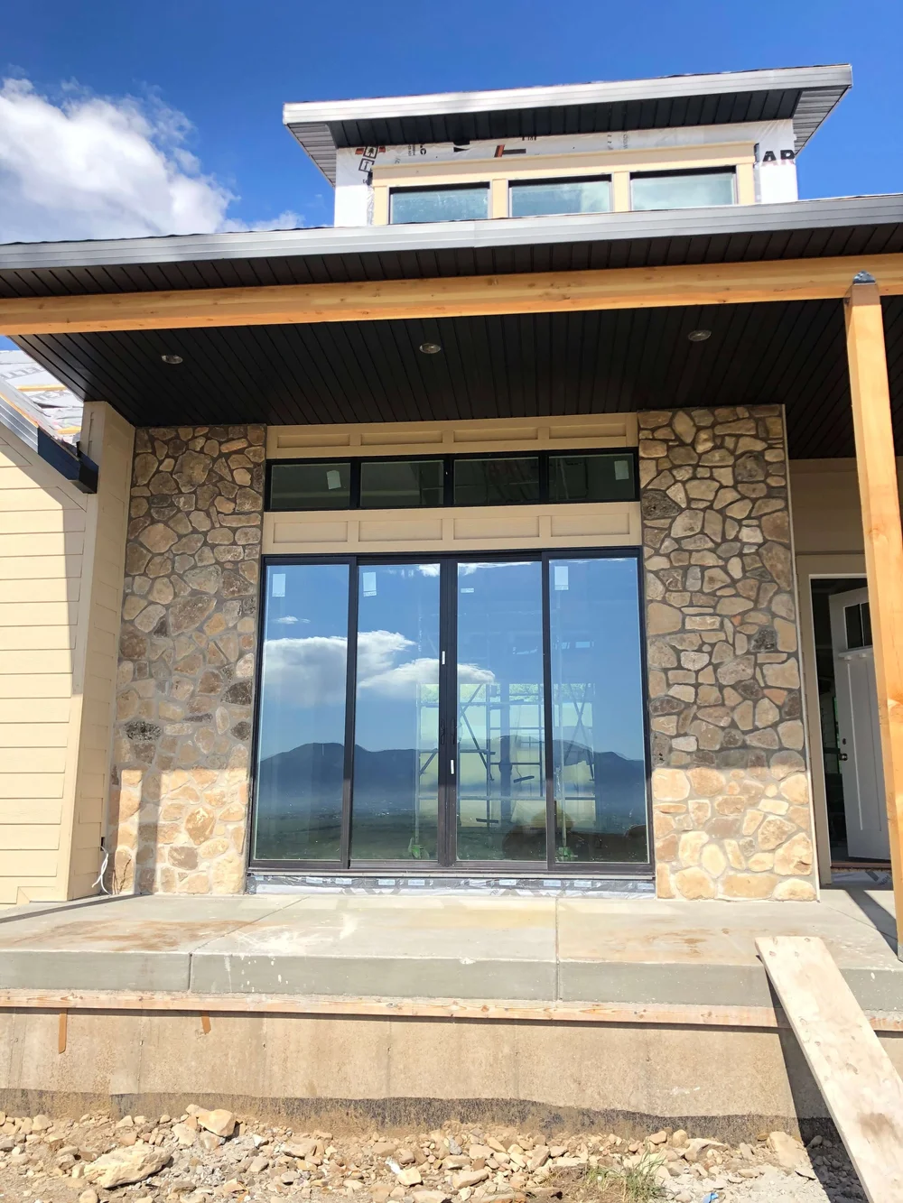 Covered entry with stone columns and full-height glass doors on a Cache Valley custom home