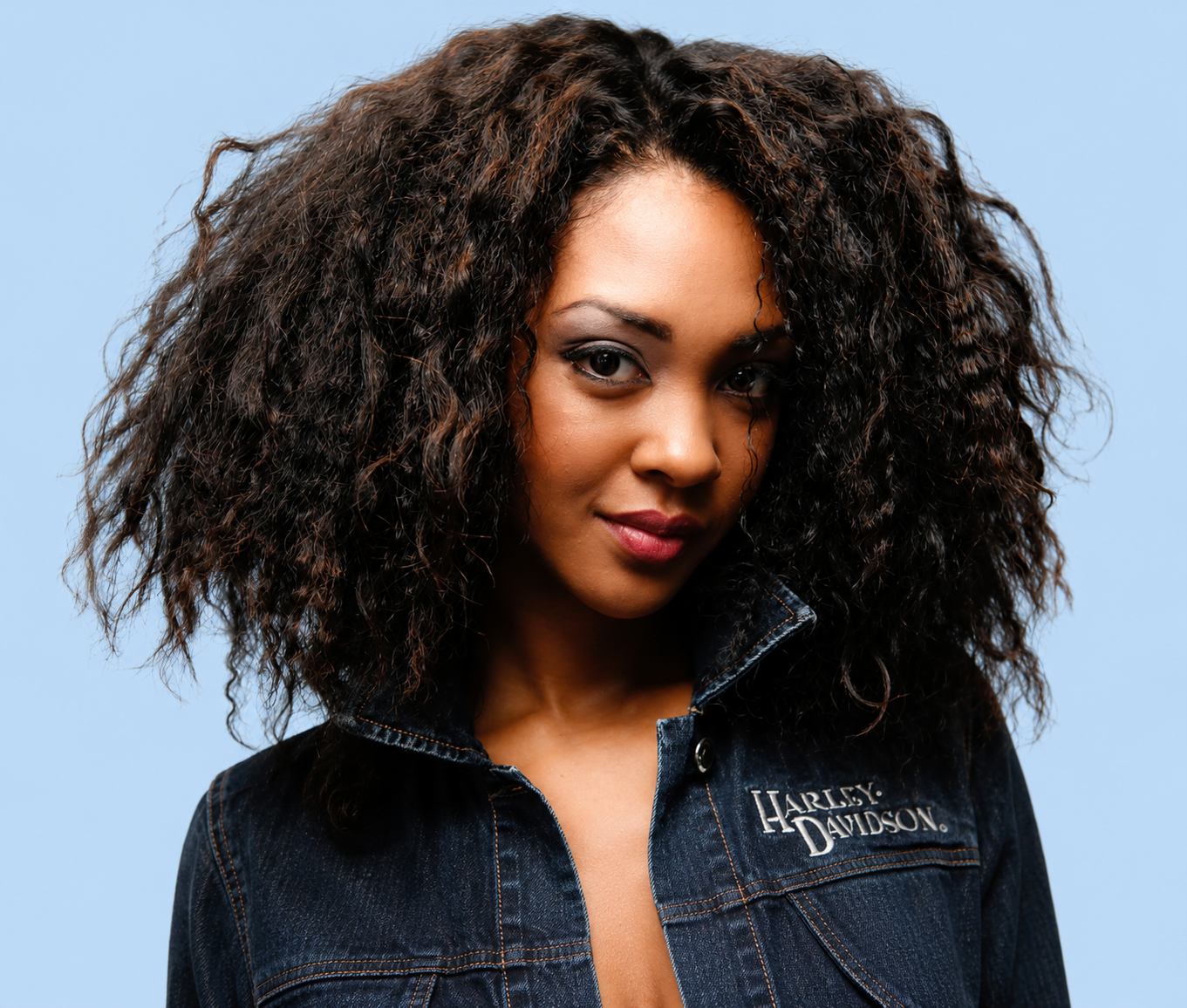 Close-up of a woman with curly hair wearing a denim jacket and Harley Davidson shirt.