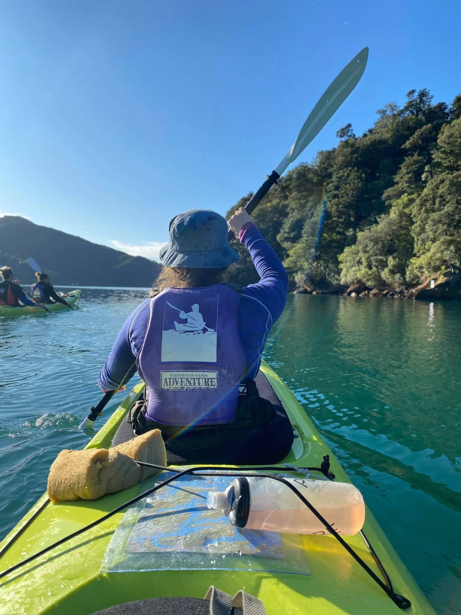 Group of kayakers paddling through clear blue water with lush green hills in Marlborough Sounds during a guided adventure.