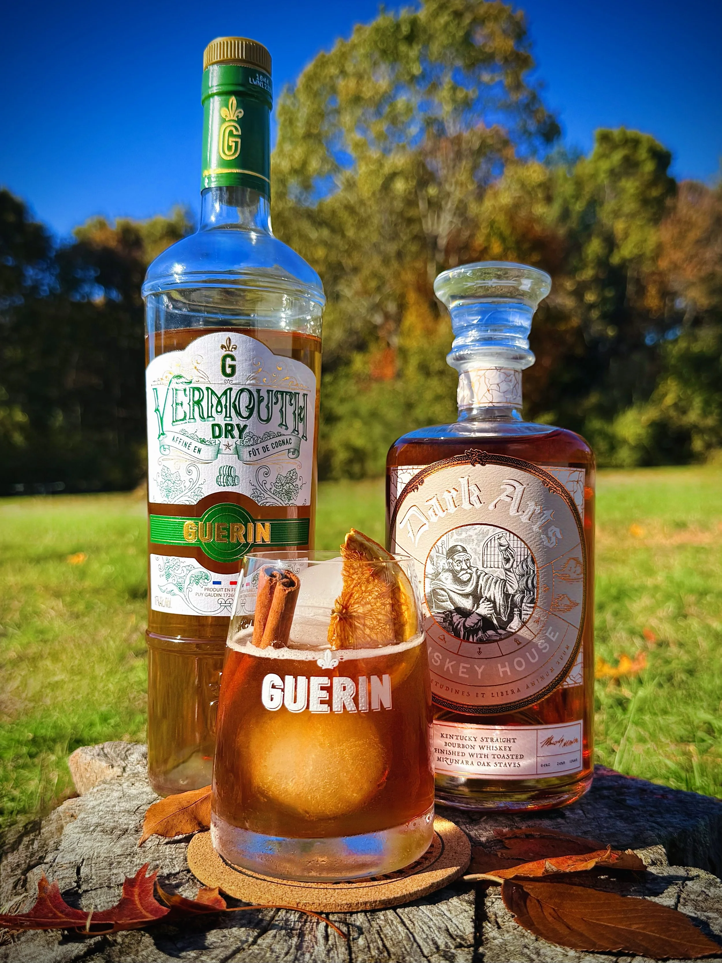 An autumnal Maple Manhattan made with Dark Arts Whiskey and Guerin Dry Vermouth. Garnished with cinnamon and orange in an outdoor fall setting—perfect for seasonal cocktail inspiration.