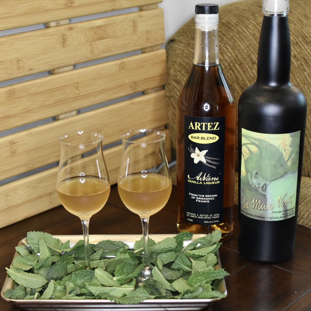 Photo of two glasses on a tray of mint with bottles behind