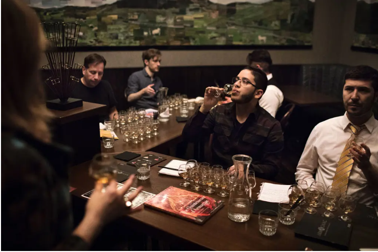 Men sitting around an L-shaped bar tasting samples of Armagnac while a woman lectures