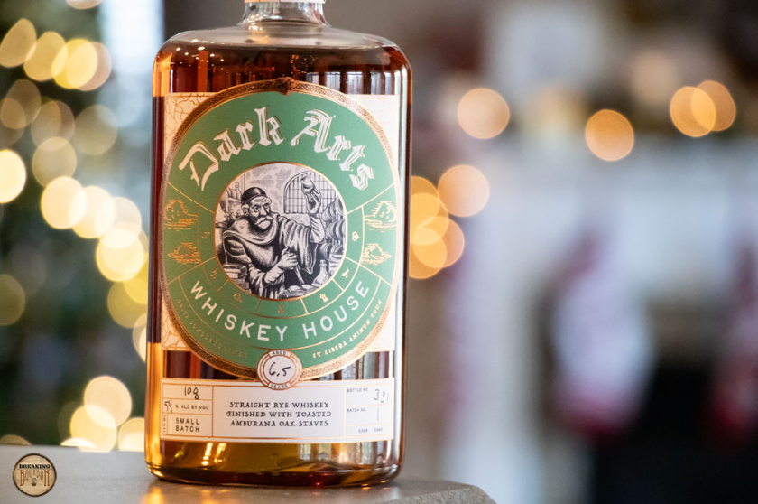 Green labeled Dark Arts Amburana Rye Whisky on a background with out of focss lights