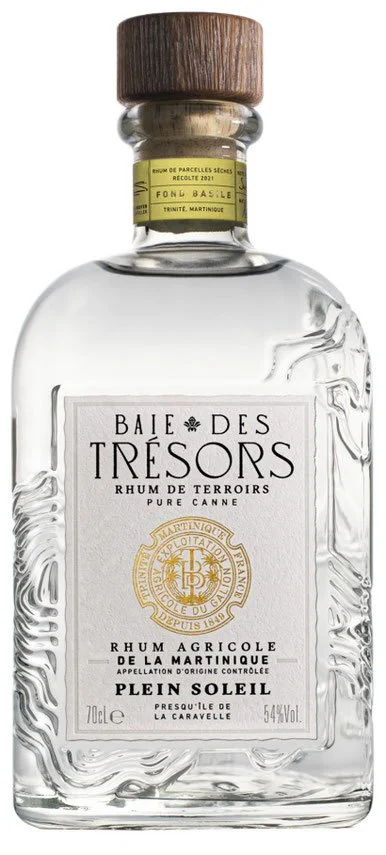 A clear square-based glass bottle of Baie des Trésors Rhum Agricole Martinique. It has a wooden cap, a yellow band near the neck, and a white label with the name Plein Soleil in black text, indicating it is 70cl with 54% alcohol by volume.