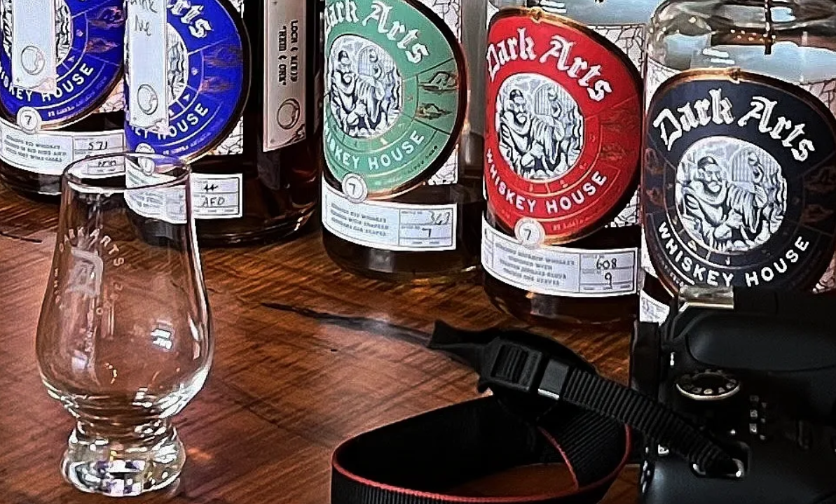 Lineup of whiskey bottles with a Glencairn glass and camera in the foreground