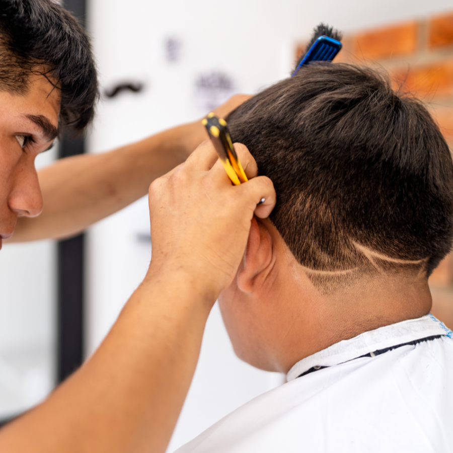 Barber giving a haircut, using scissors and a comb to style a man's hair inside a barber shop.