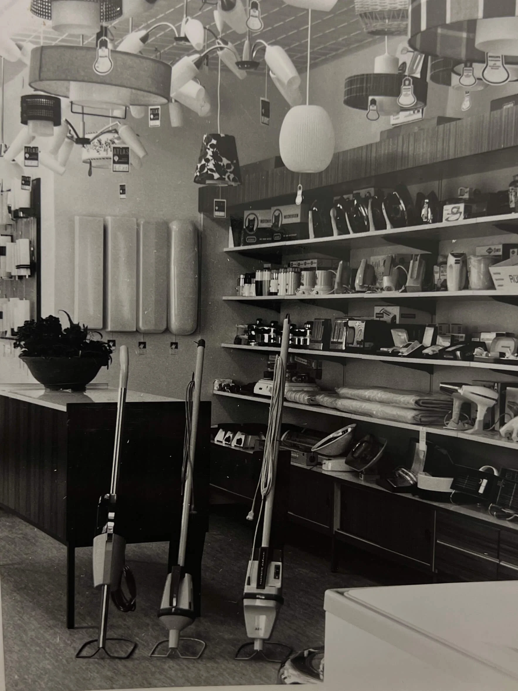 Ein Elektrofachgeschäft mit Staubsaugern, Bügeleisen, Küchenmaschinen und Lampen. Es sind mehrere Staubsauger auf den Boden gestellt und Regale mit Haushaltsgeräten an der Wand.