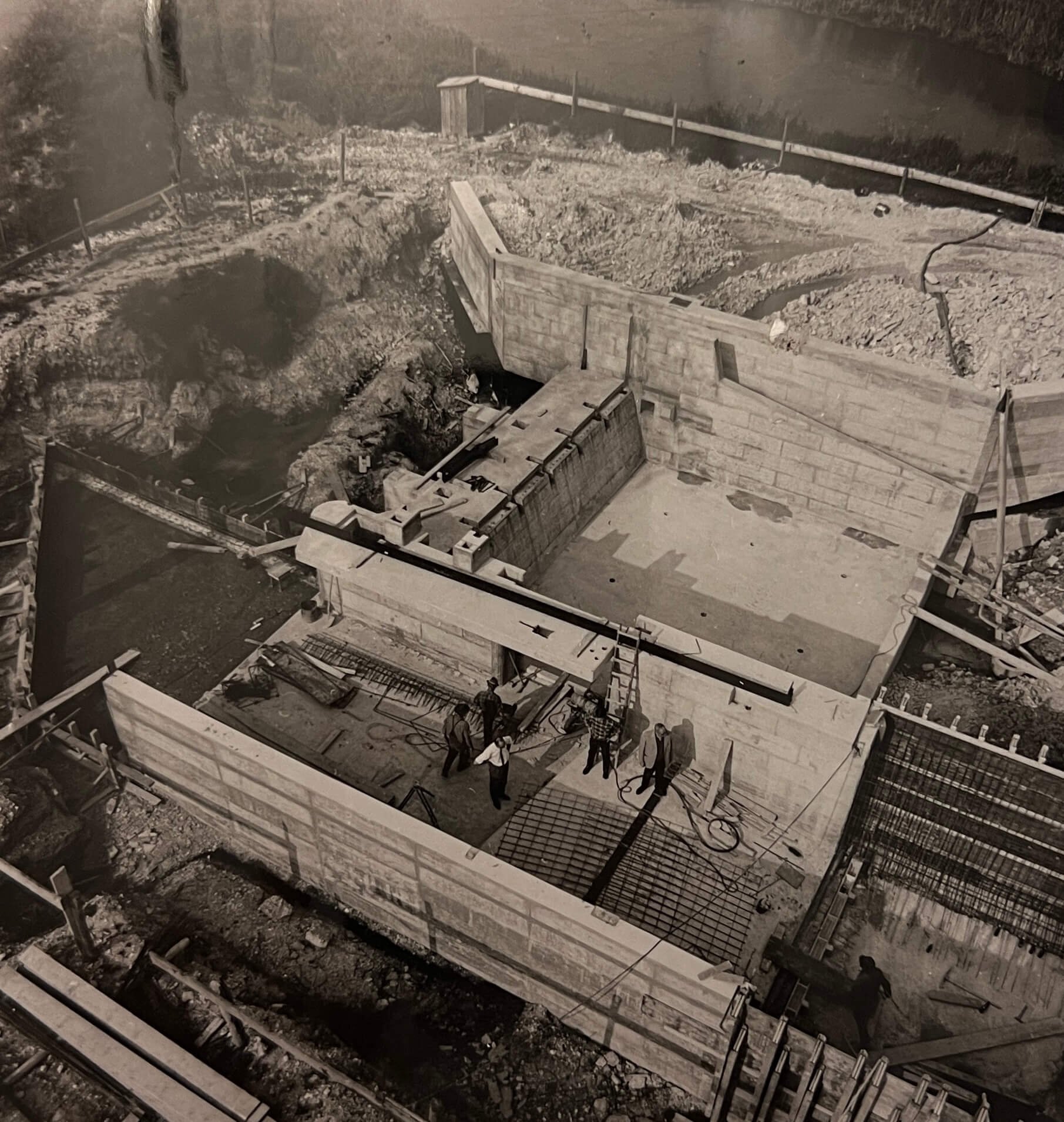 Bauarbeiter und Bauarbeiterinnen sind auf einer Baustelle, die mit Betonwänden und Eisen verstärkt ist, während das Fundament eines Gebäudes gebaut wird.