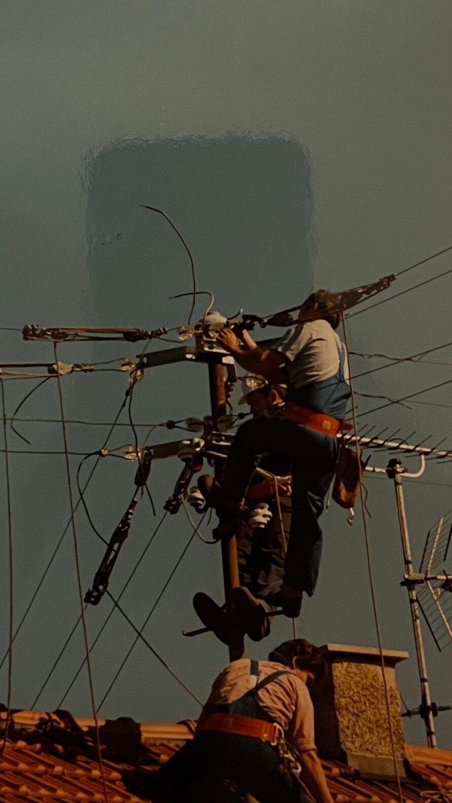 Drei Arbeiter auf einem Strommast, die an einer Antenne arbeiten, bei Nacht mit dunklem Himmel im Hintergrund.