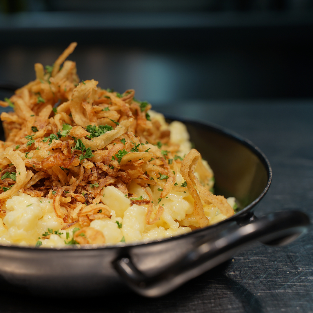 Ein Gericht mit Kartoffeln, Zwiebeln, knusprigen Zwiebelringen und frischer Petersilie in einer schwarzen Pfanne