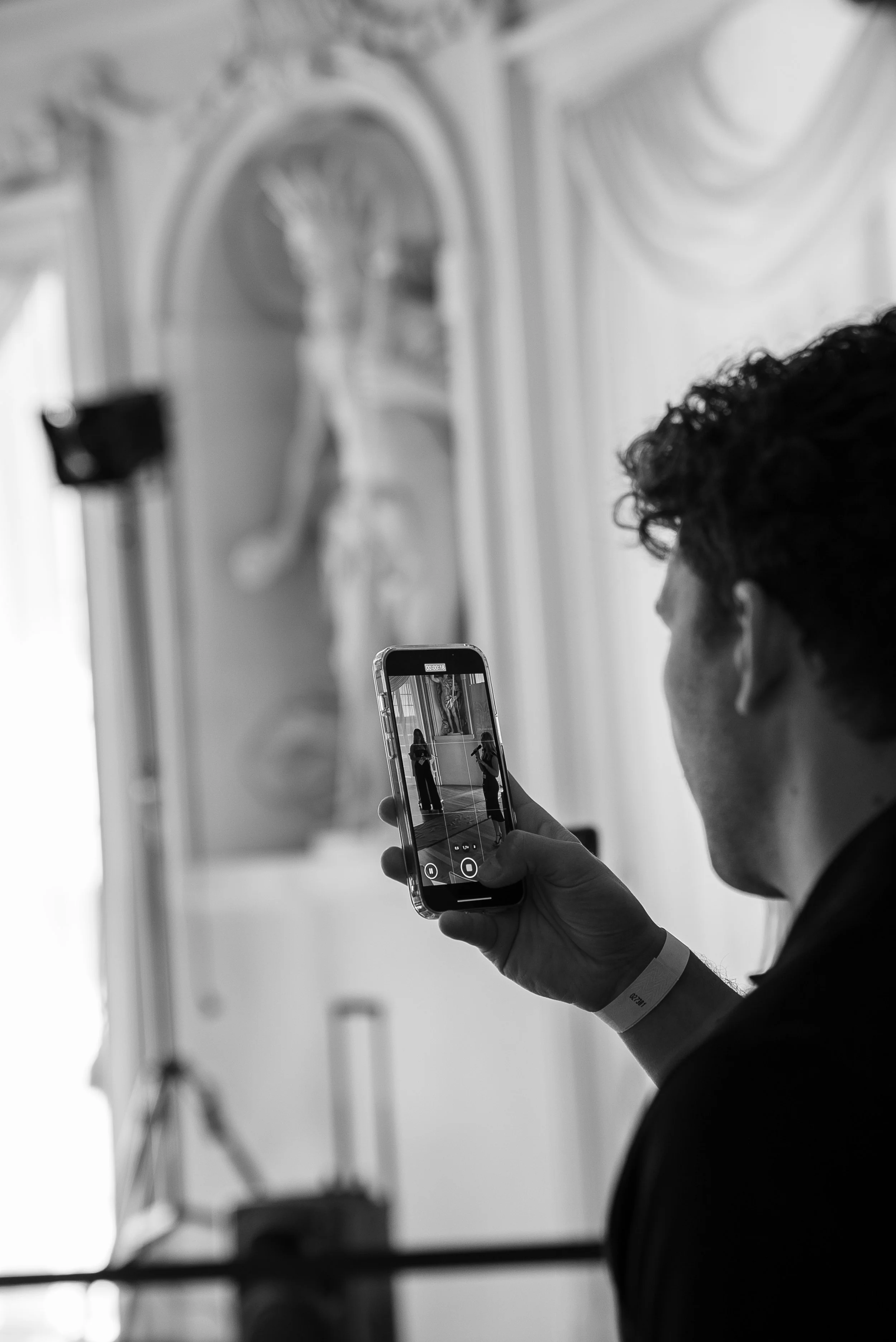 Ein Mann nimmt ein Foto oder Video mit einem Smartphone von einer Skulptur in einem Museum auf, das auf einer Bühne steht.