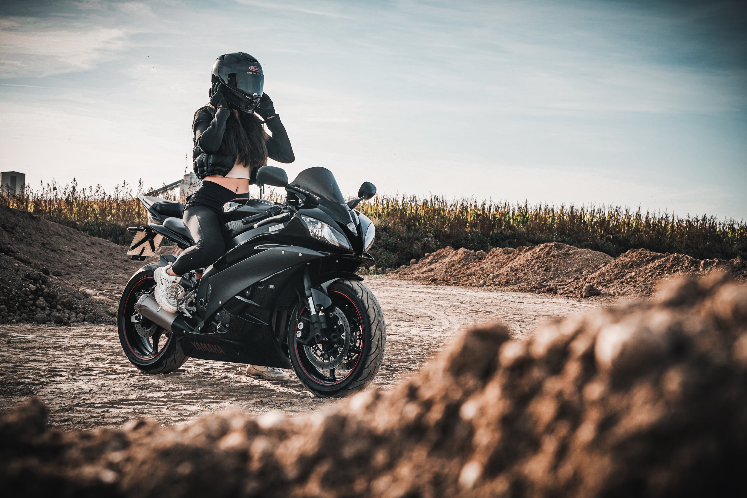 Frau in Motorradhelm und Lederjacke auf schwarzem Sportmotorrad auf unbefestigtem Feldweg