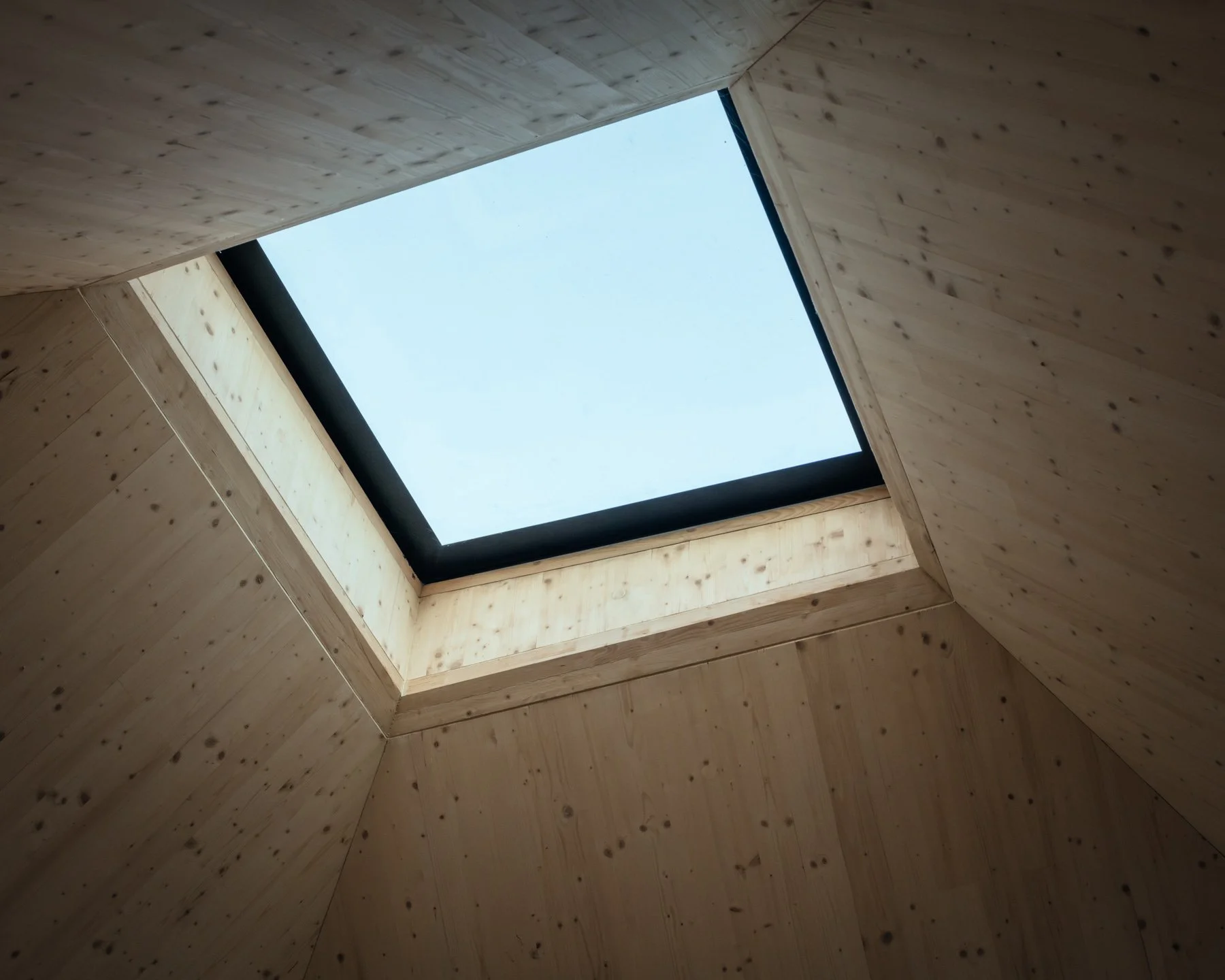 Looking up at a square skylight in a wooden ceiling, with sky visible through the opening.