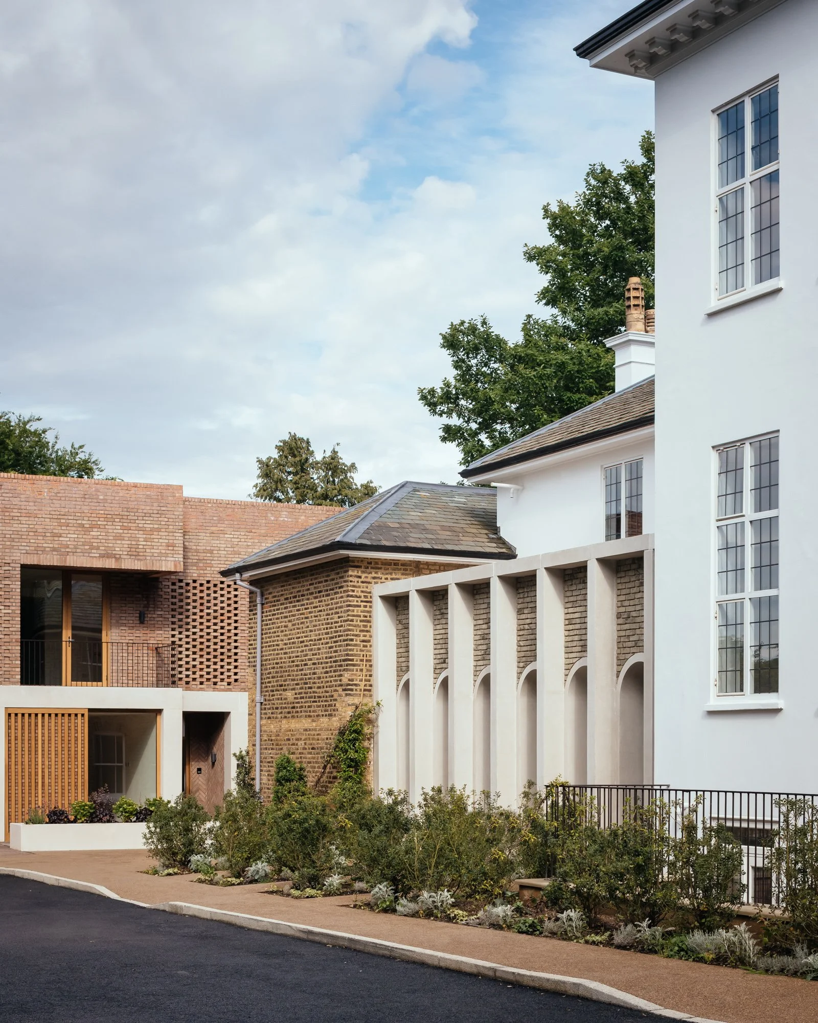 Residential buildings with modern architecture, brick and white exterior walls, large windows, and landscaped garden with shrubs, plants, and a paved walking path.