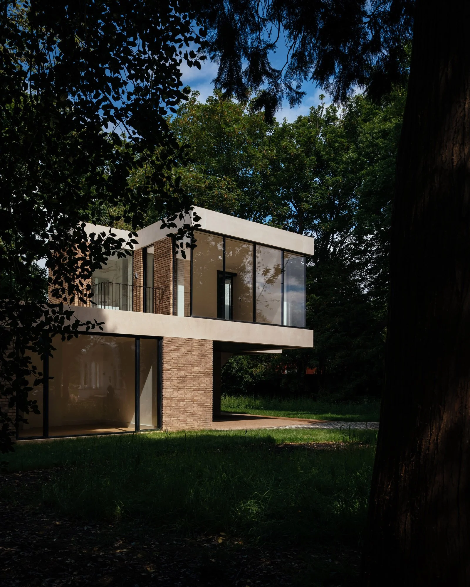 Modern two-story house with large glass windows, surrounded by trees and greenery, during daytime.