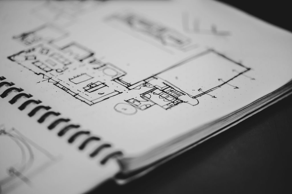 Architectural blueprint on desk with black coffee mug, color swatch samples, marble tile sample, and potted plants.