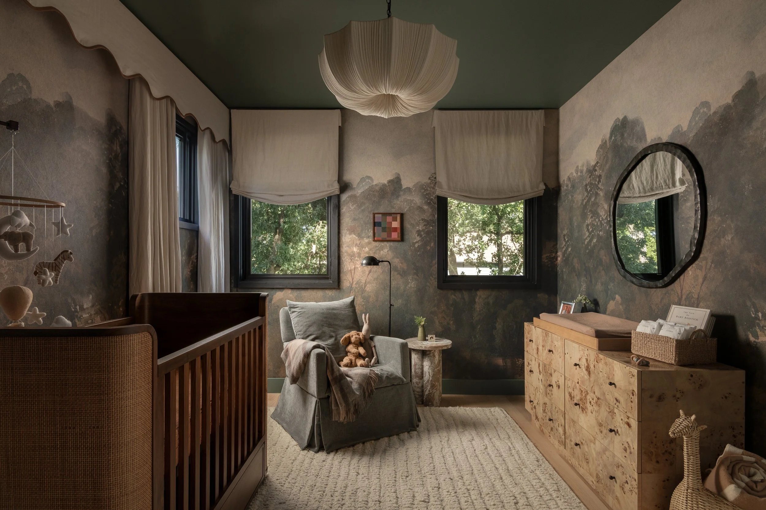 A serene and stylish nursery featuring soft, neutral tones, a crib, cozy armchair, and natural wood dresser, with a beautiful landscape mural on the walls and large windows letting in natural light.