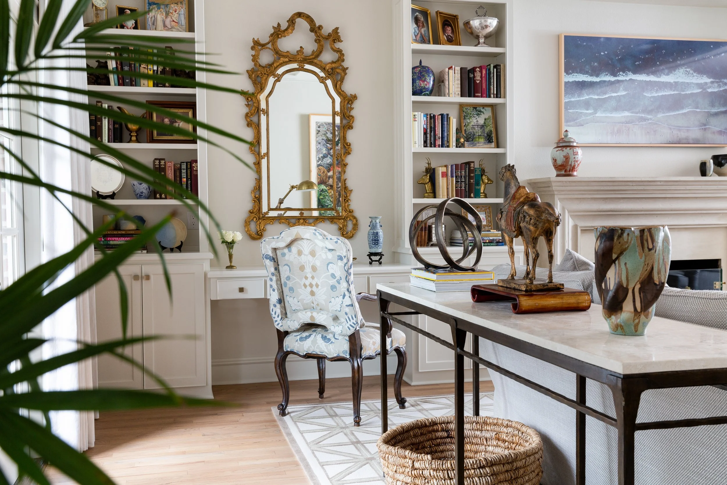 A stylish living room featuring a vintage gold-framed mirror, a marble-topped console table, decorative sculptures, and bookshelves filled with colorful books, creating an elegant and cozy space by Austin Interior Photography